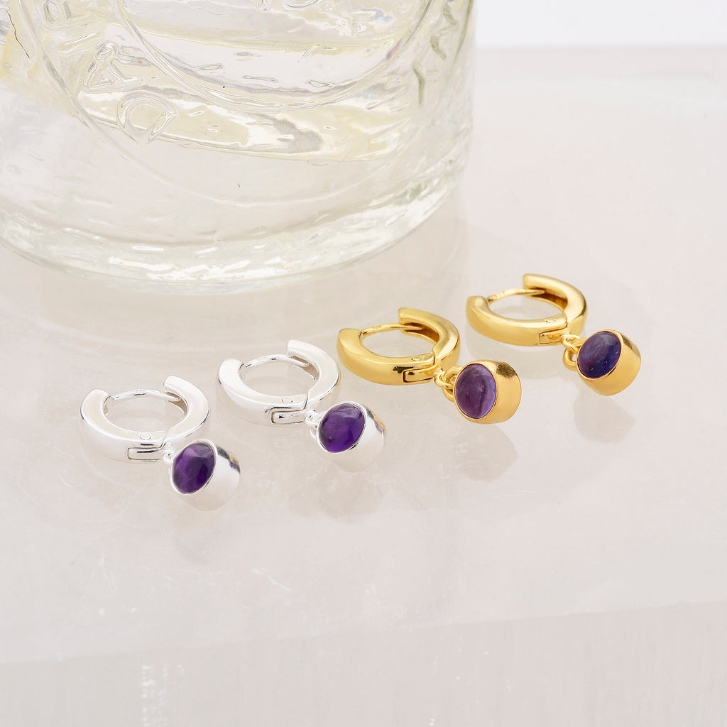 two pairs or amethyst birthstone hoops next to a jar