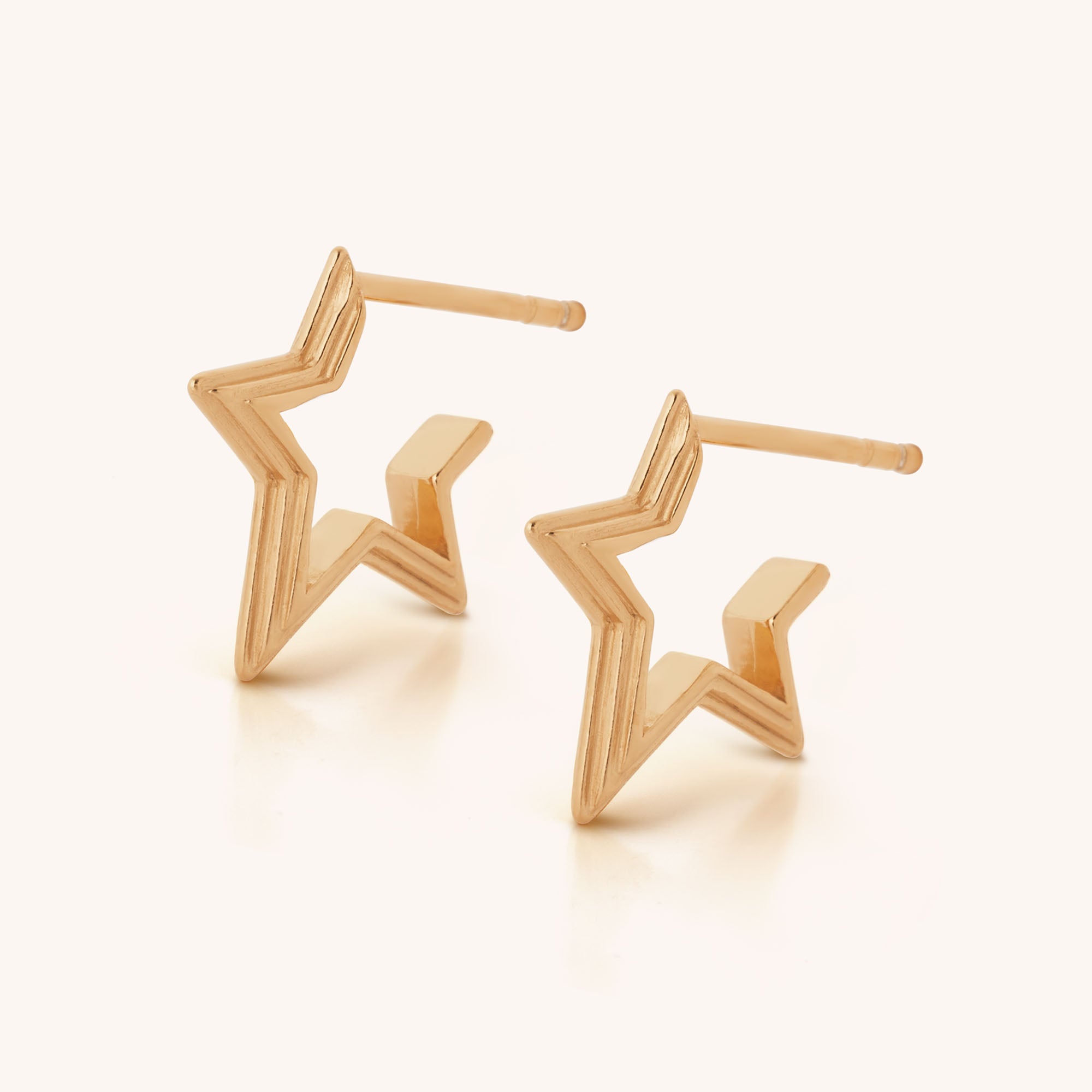 The Stellar Hoop Earrings are gold, star-shaped with a zigzag design, radiating celestial charm and displayed on a light background.