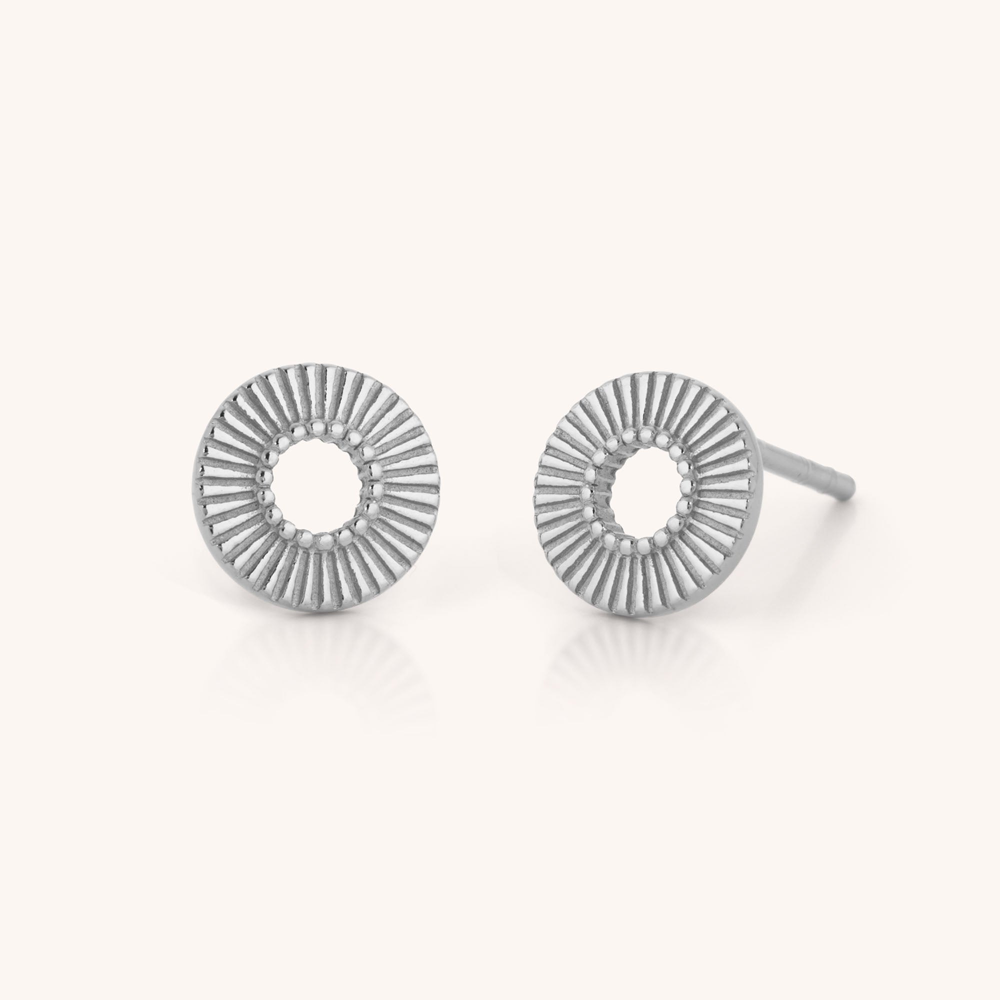 Solar Circle Earrings in sterling silver, featuring open circles with a radiating sunburst pattern, capture celestial elegance on a simple light background.