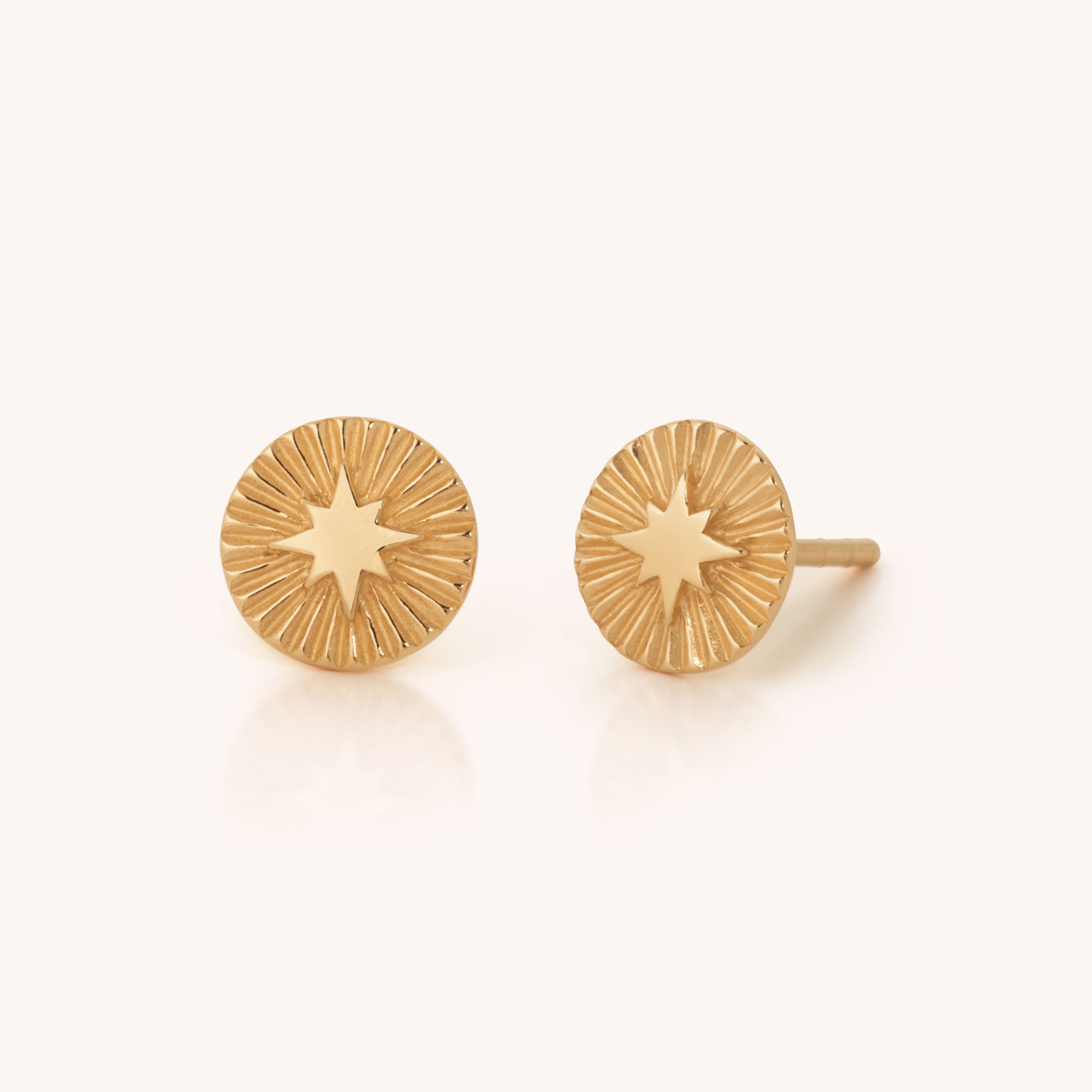Shining Star Stud Earrings: round gold studs featuring a raised star at the center with engraved sunburst rays radiating outward.