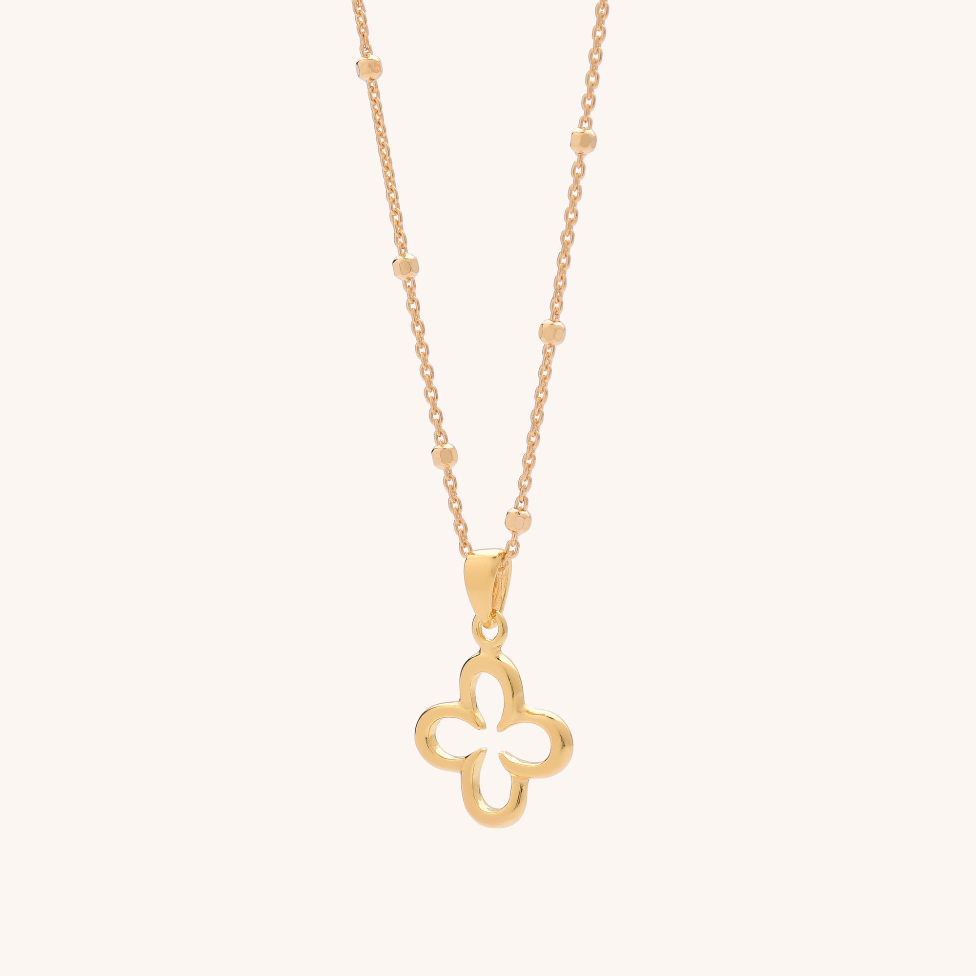 The Clover Necklace features a delicate gold beaded chain and a hollow four-leaf clover pendant, displayed on a light beige background—a standout accessory for any jewellery collection.