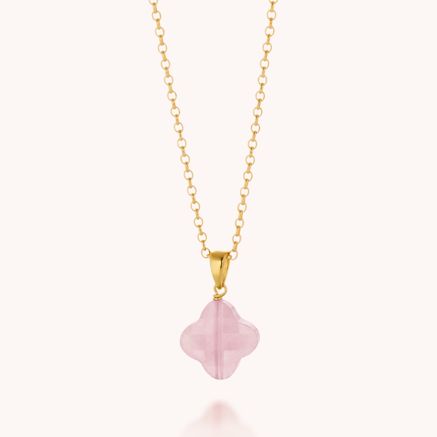 The Gem Clover Necklace features a translucent pink, clover-shaped gemstone pendant set in a simple gold bail, shown against a plain light background.