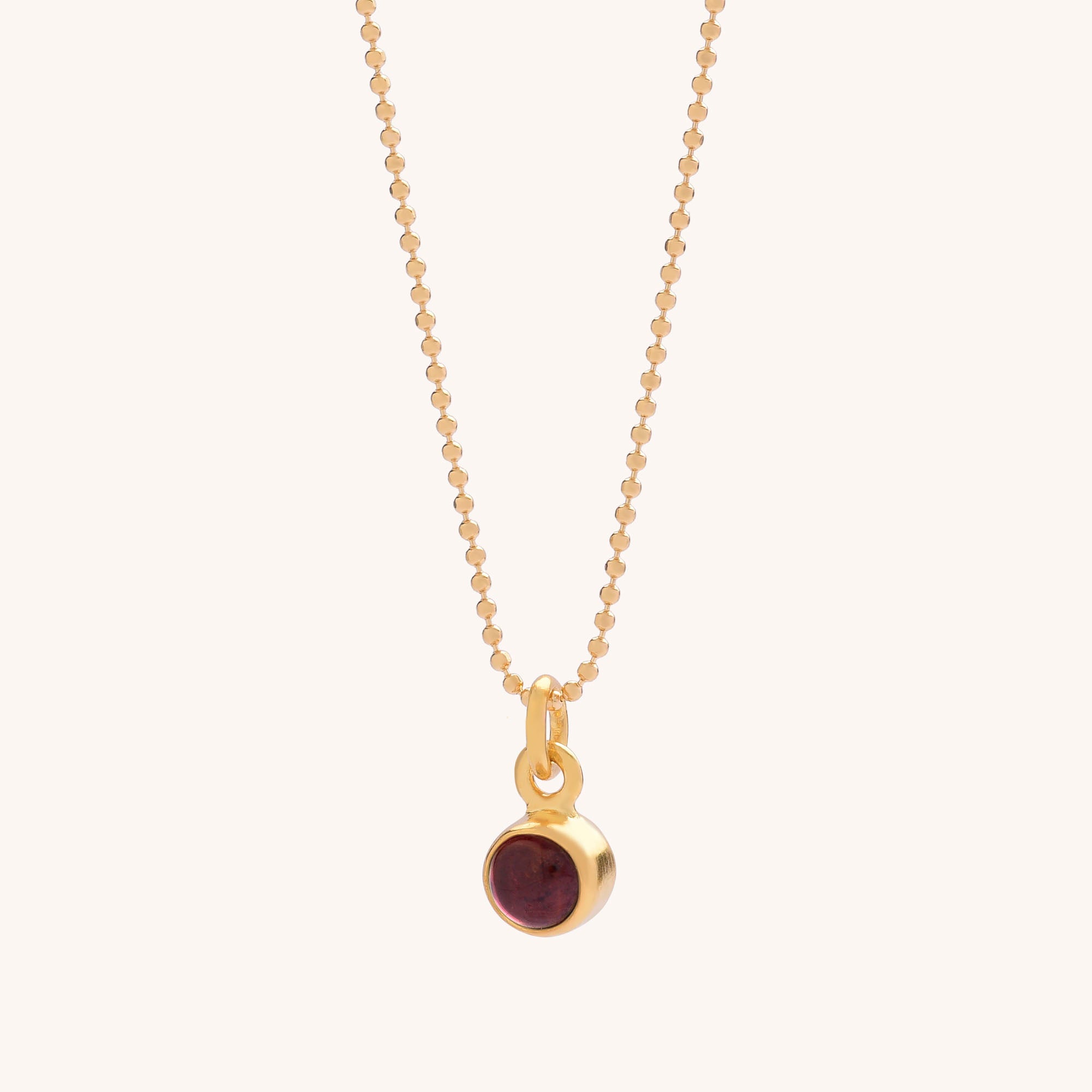 The Gem Dot Birthstone Necklace January features a delicate gold beaded chain and a small round Garnet pendant in a simple gold bezel, offering understated elegance—ideal for those who love subtle style.