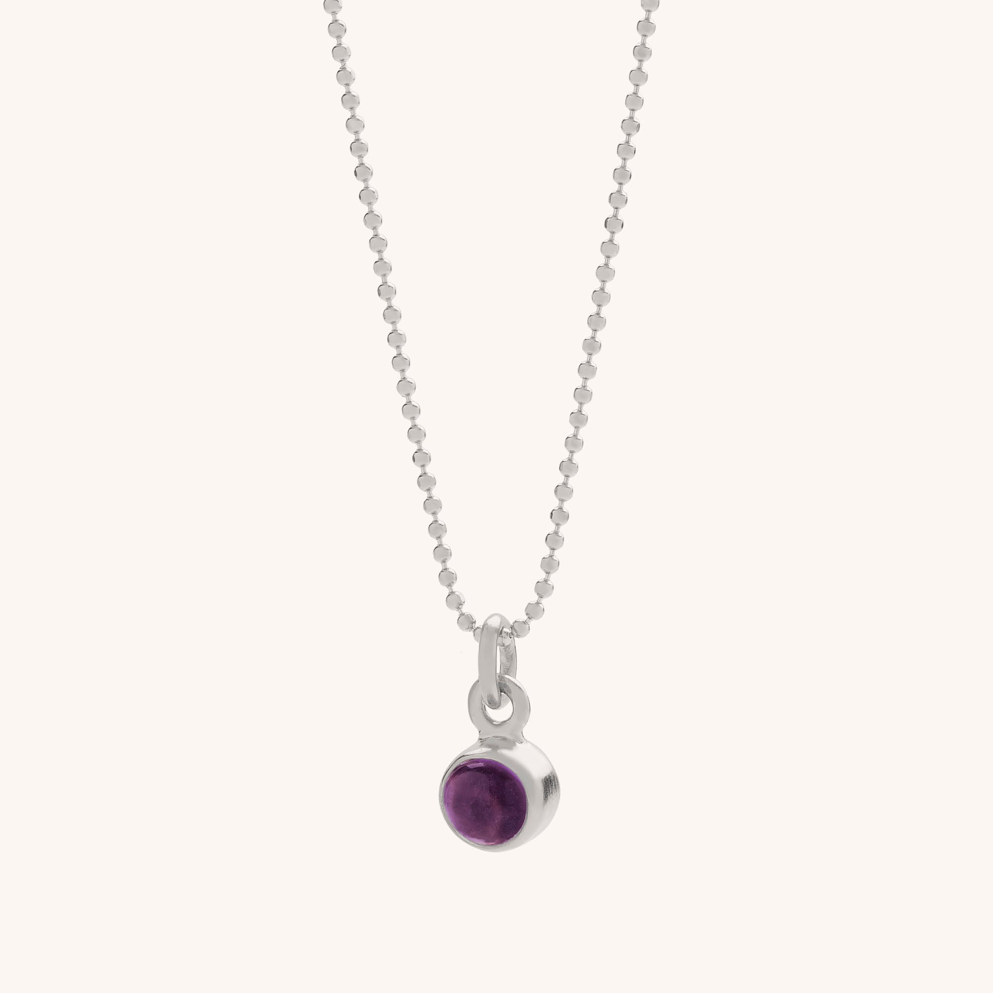 The Gem Dot Birthstone Necklace February features a delicate silver ball chain and a small round pendant with a deep purple amethyst in a simple bezel, making it ideal as a birthstone necklace or for its calming qualities.