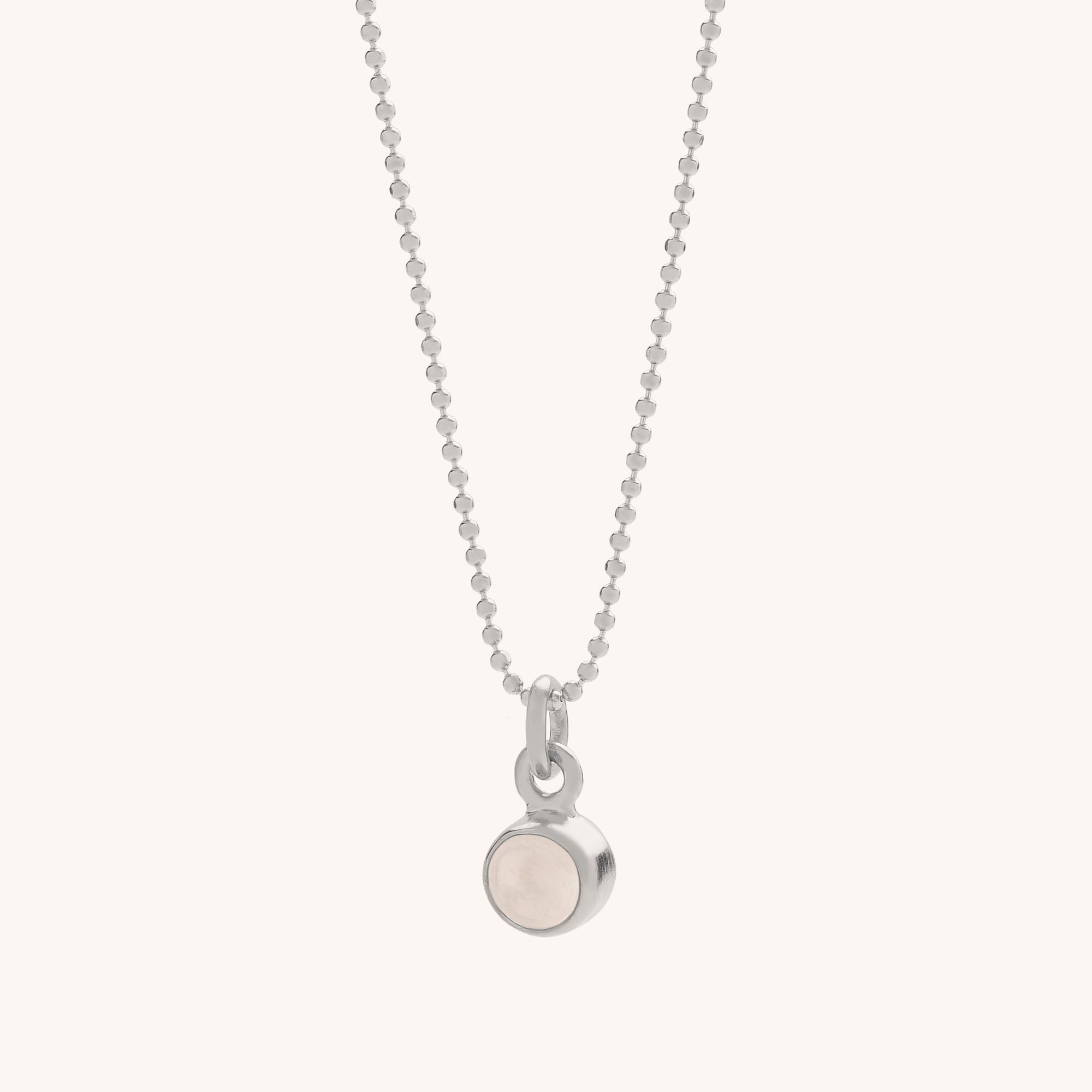 The Gem Dot Birthstone Necklace April features a round, bezel-set pale crystal gemstone pendant on an eco-silver beaded chain, displayed against an off-white background.