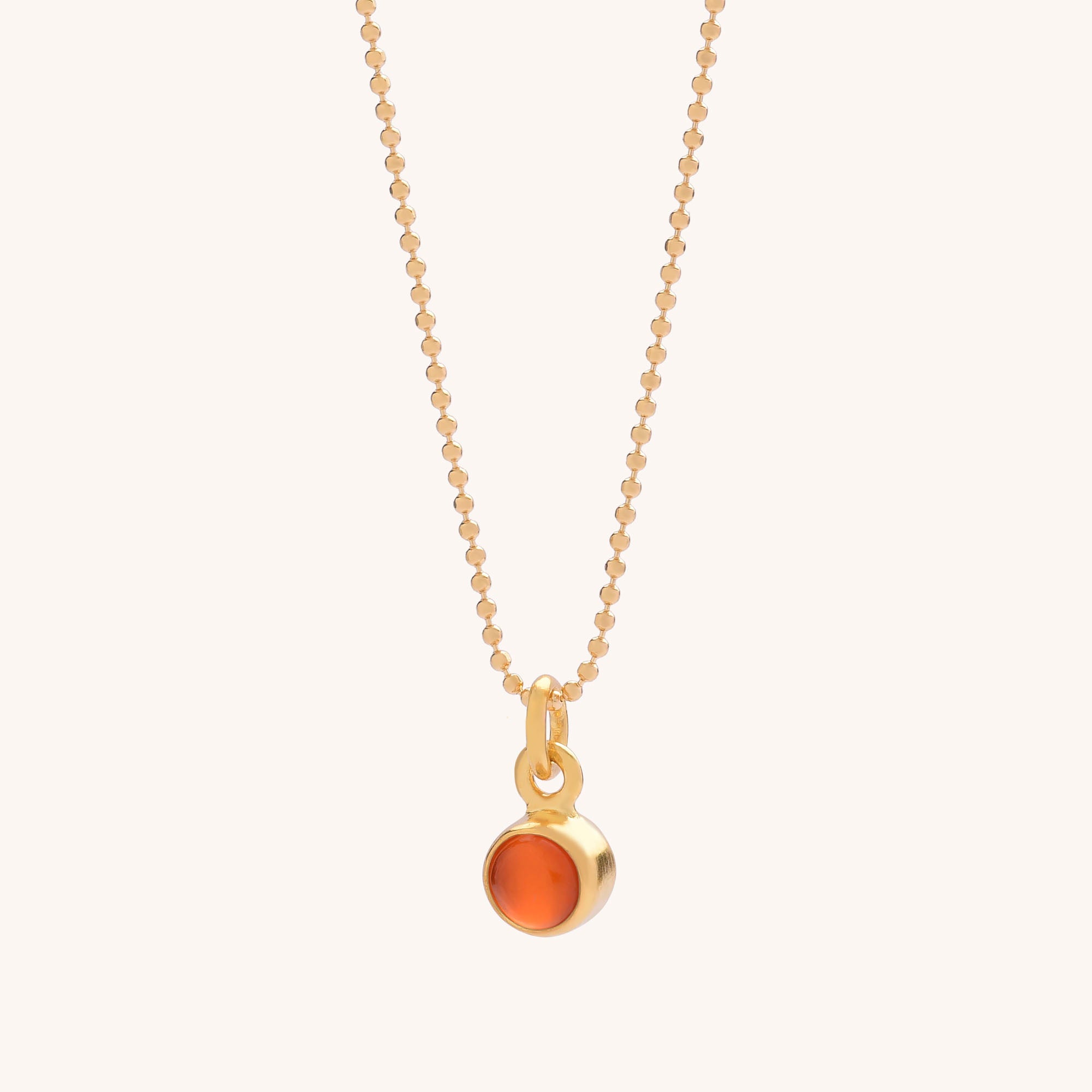 The Gem Dot Birthstone Necklace July features a gold beaded chain with a small round carnelian pendant set in gold, displayed against a simple light background.