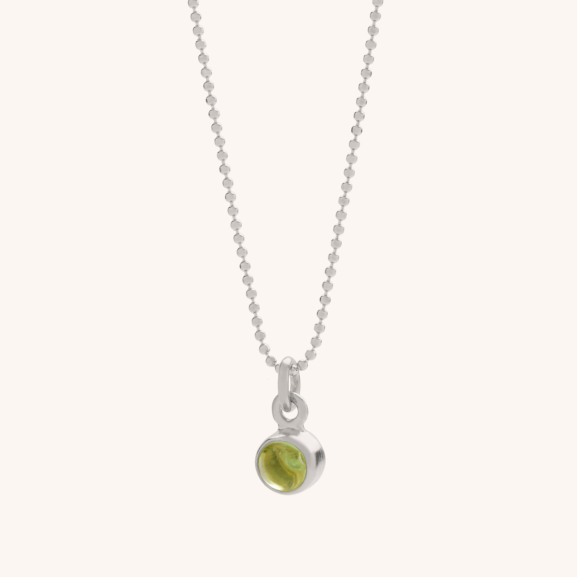 The Gem Dot Birthstone Necklace August features a delicate silver beaded chain and a small round peridot gemstone in a simple silver bezel—an elegant accessory for any occasion.