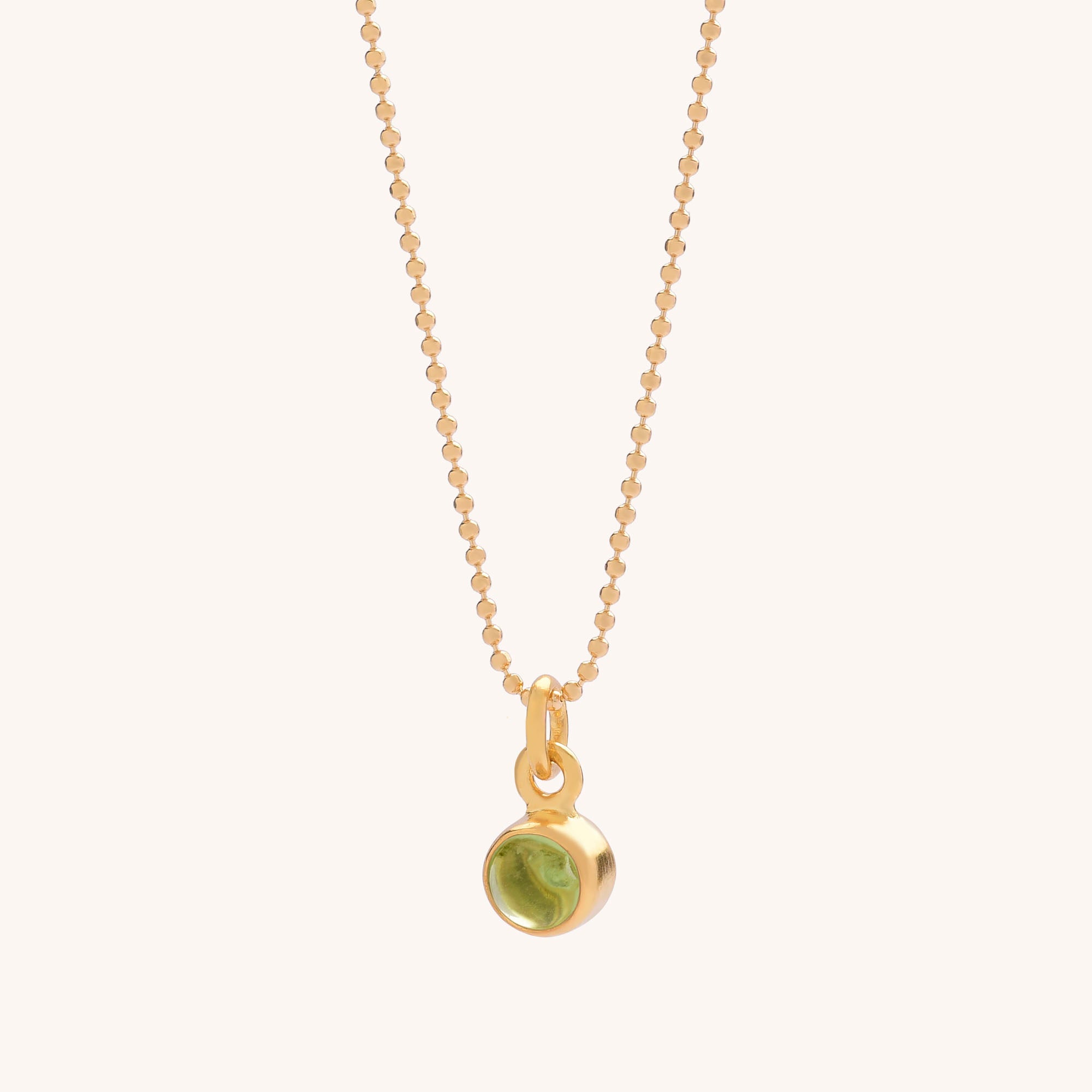 The Gem Dot Birthstone Necklace August features a delicate gold chain with a small, round Peridot gemstone pendant in a gold bezel, displayed on a simple light background.
