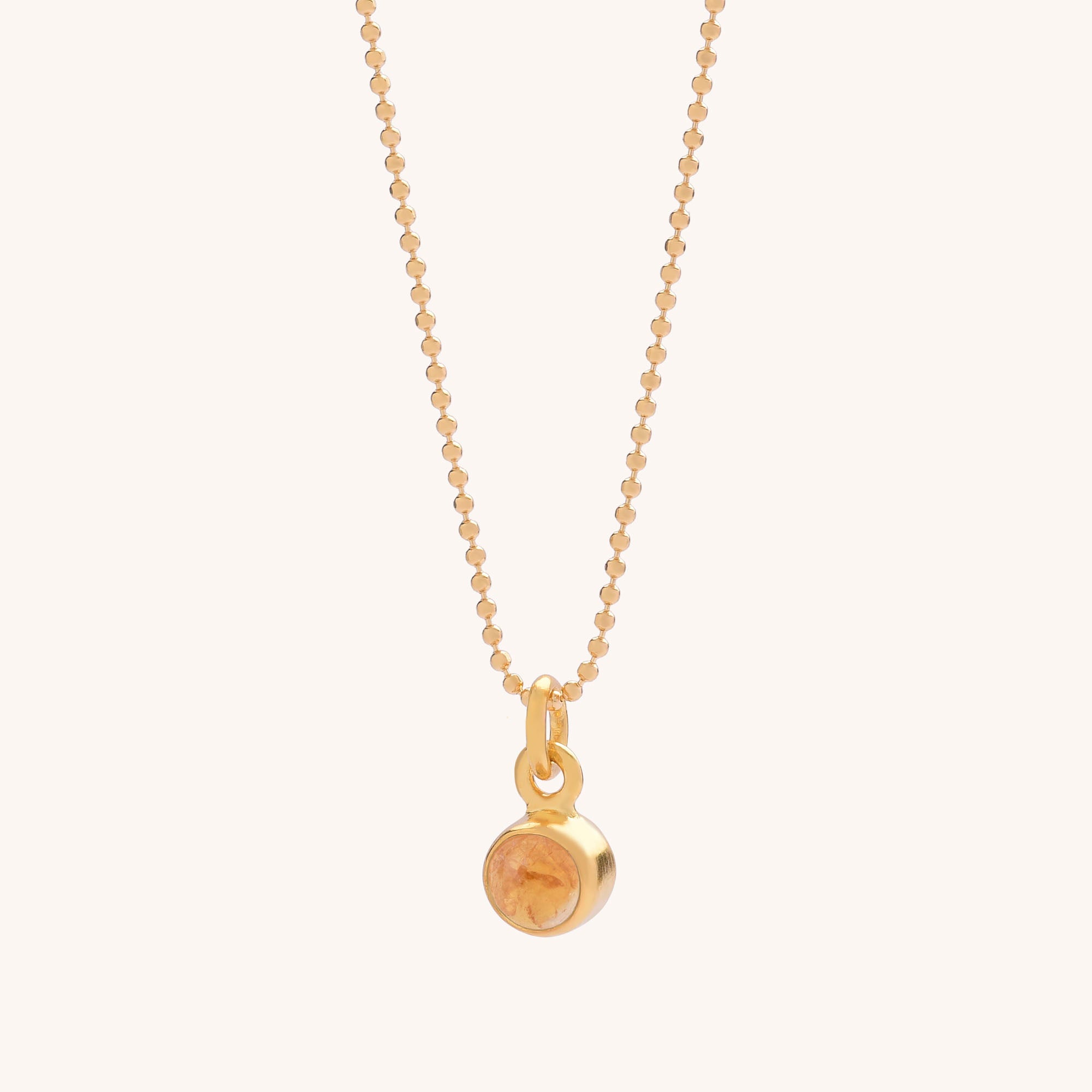 The Gem Dot Birthstone Necklace November features a gold beaded chain with a small round Citrine pendant, the November birthstone, displayed on an off-white background.