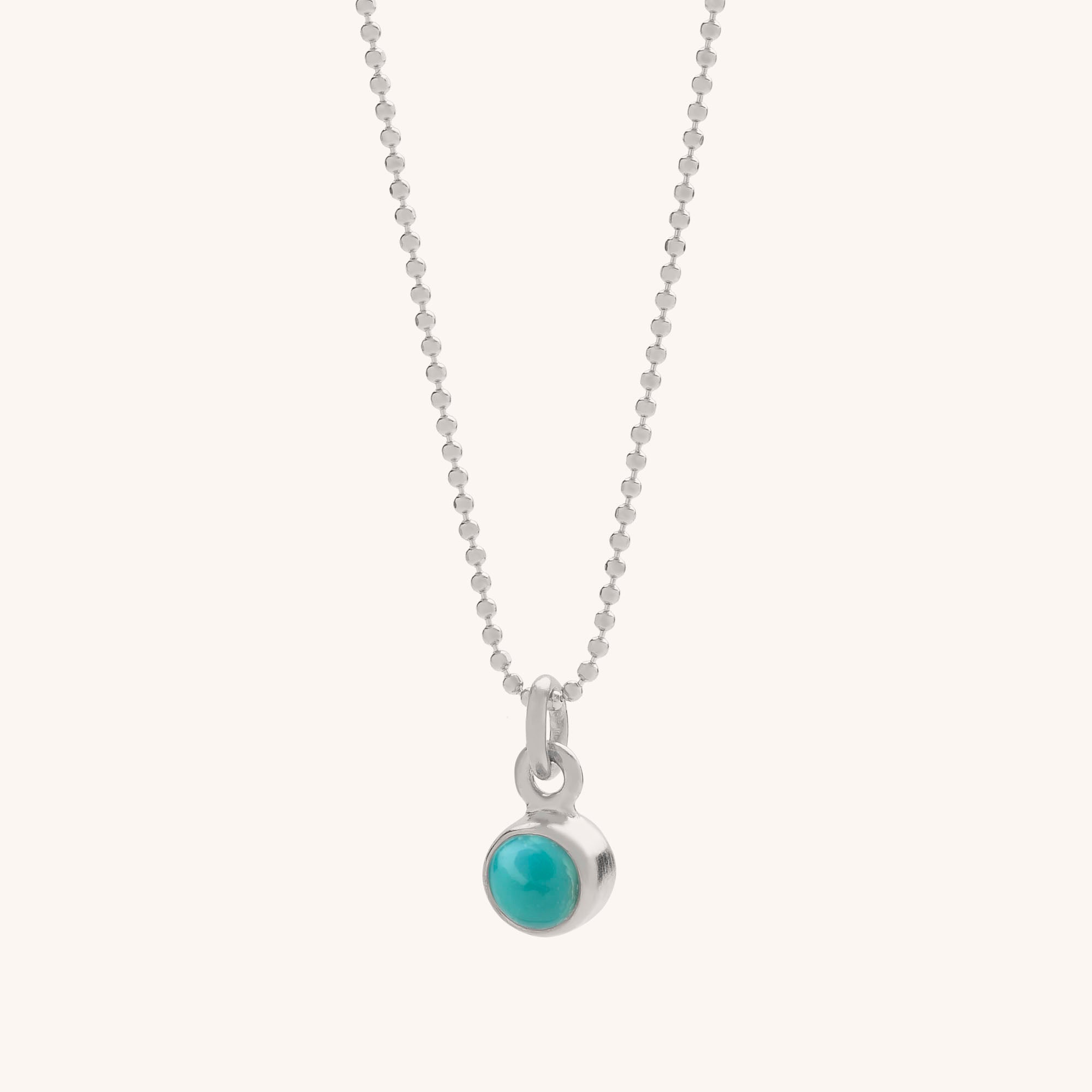 The Gem Dot Birthstone Necklace December features a delicate silver chain with a small round turquoise gemstone pendant in a simple bezel, displayed against a plain light background.