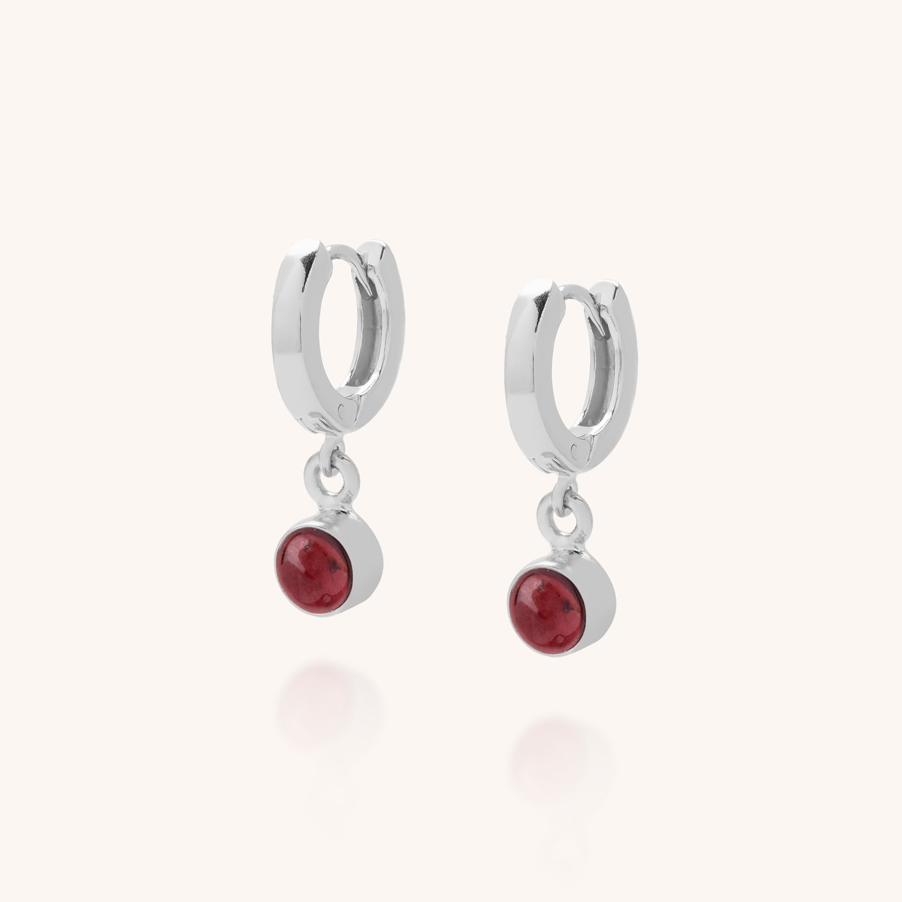 Gem Hoop Birthstone Earrings January: Sterling silver hoops each feature a small round garnet birthstone pendant, shown against a simple light background.