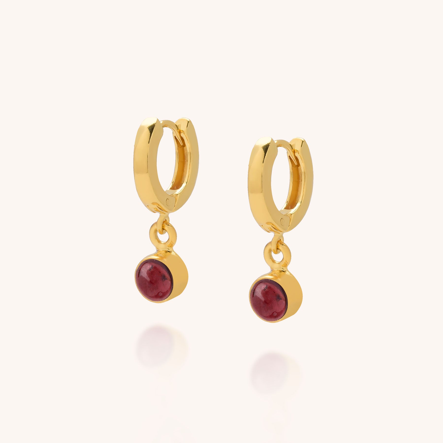 Gem Hoop Birthstone Earrings January, featuring gold hoops with small red gemstone charms reminiscent of garnet, are displayed against a light background.