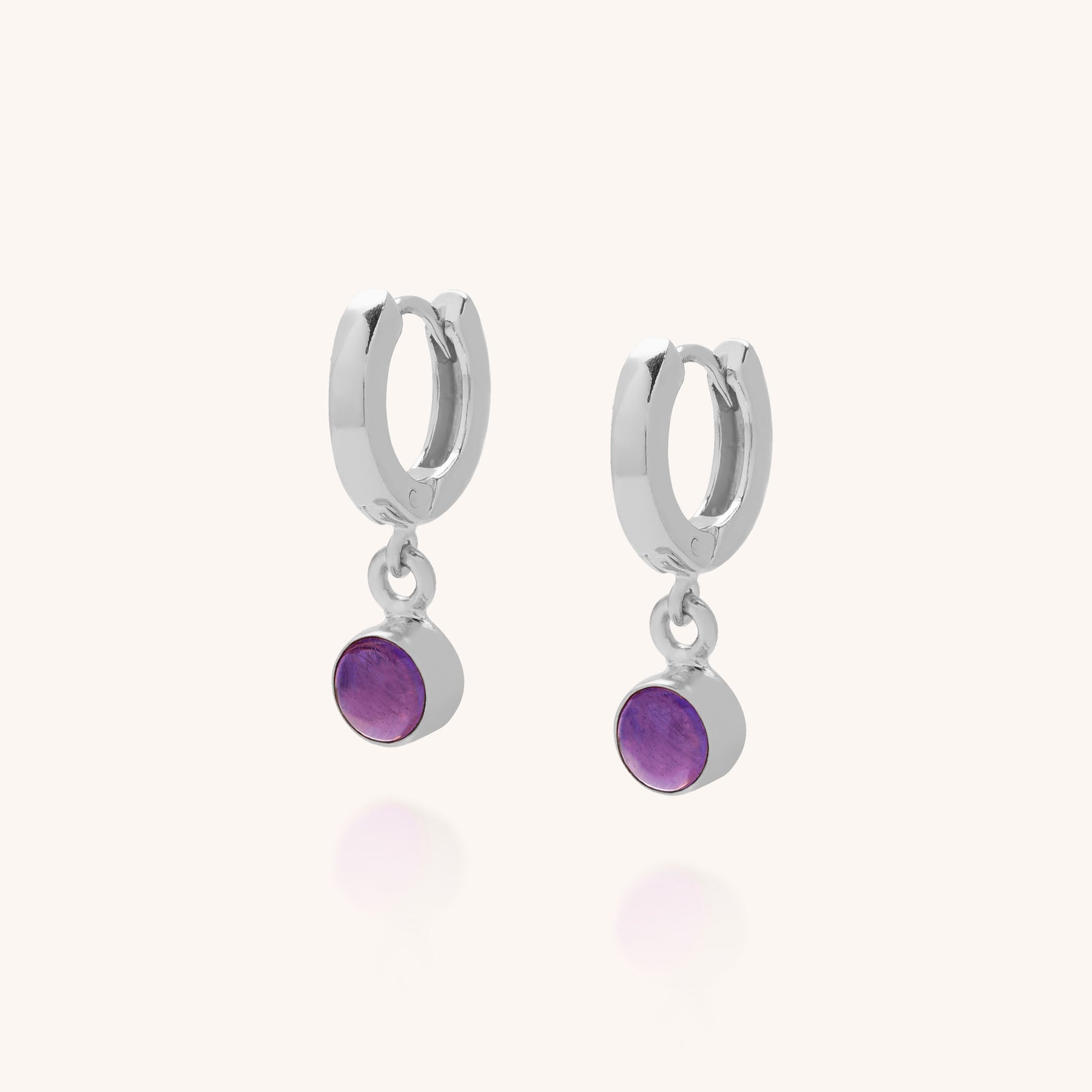 The Gem Hoop Birthstone Earrings are sterling silver hoops featuring small round natural purple gemstone charms, shown against a plain white background.