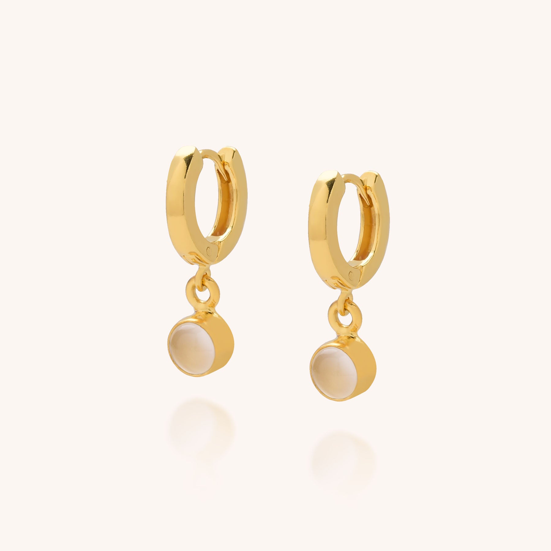 The Gem Hoop Birthstone Earrings are small gold hoops, each featuring a round, white pearl-like charm, shown against a plain light background.