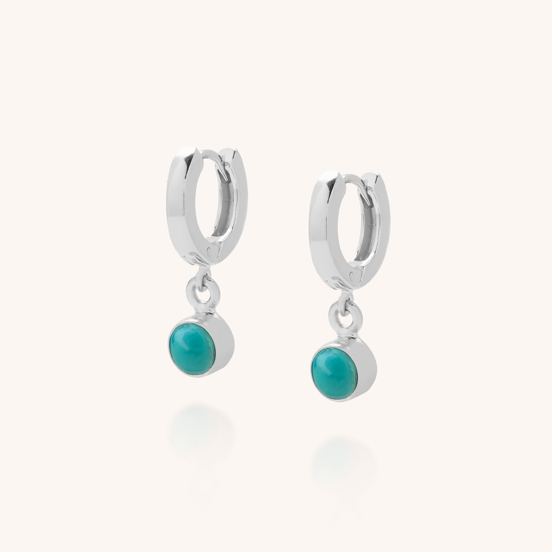 The Gem Hoop Birthstone Earrings are small sterling silver hoops with dangling round natural turquoise gemstones in silver bezels, displayed on a light background.