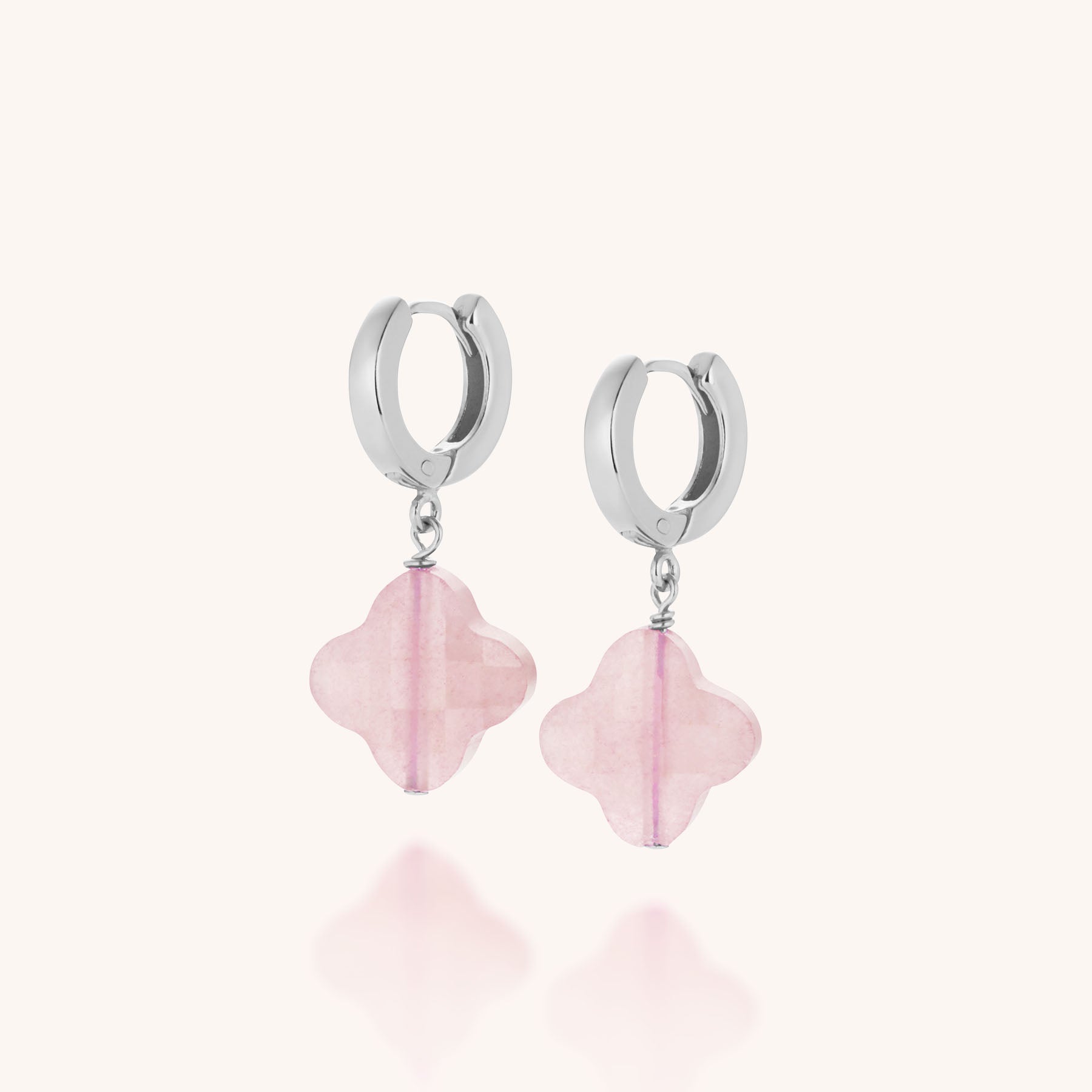 The Clover Gem Hoop Earrings feature sterling silver hoops with dangling pink, four-petal flower-shaped gemstones, shown on a light neutral background.