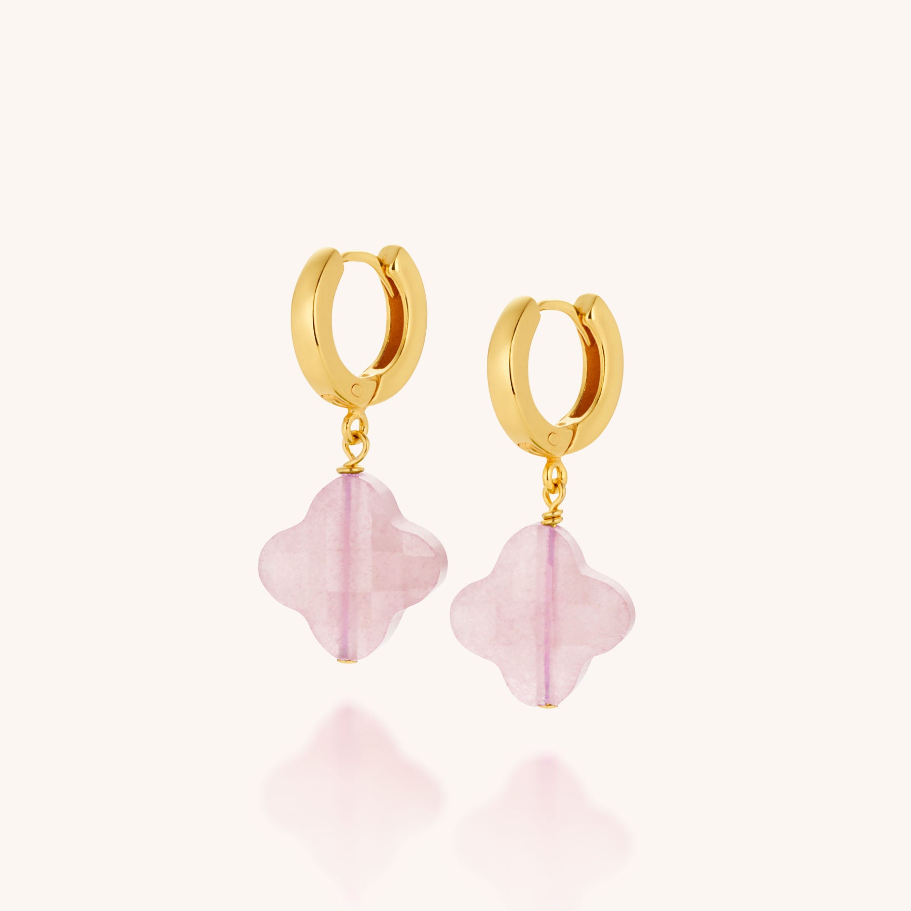 The Clover Gem Hoop Earrings feature gold hoops with dangling translucent pink gemstone quatrefoil charms, shown against a plain light background.