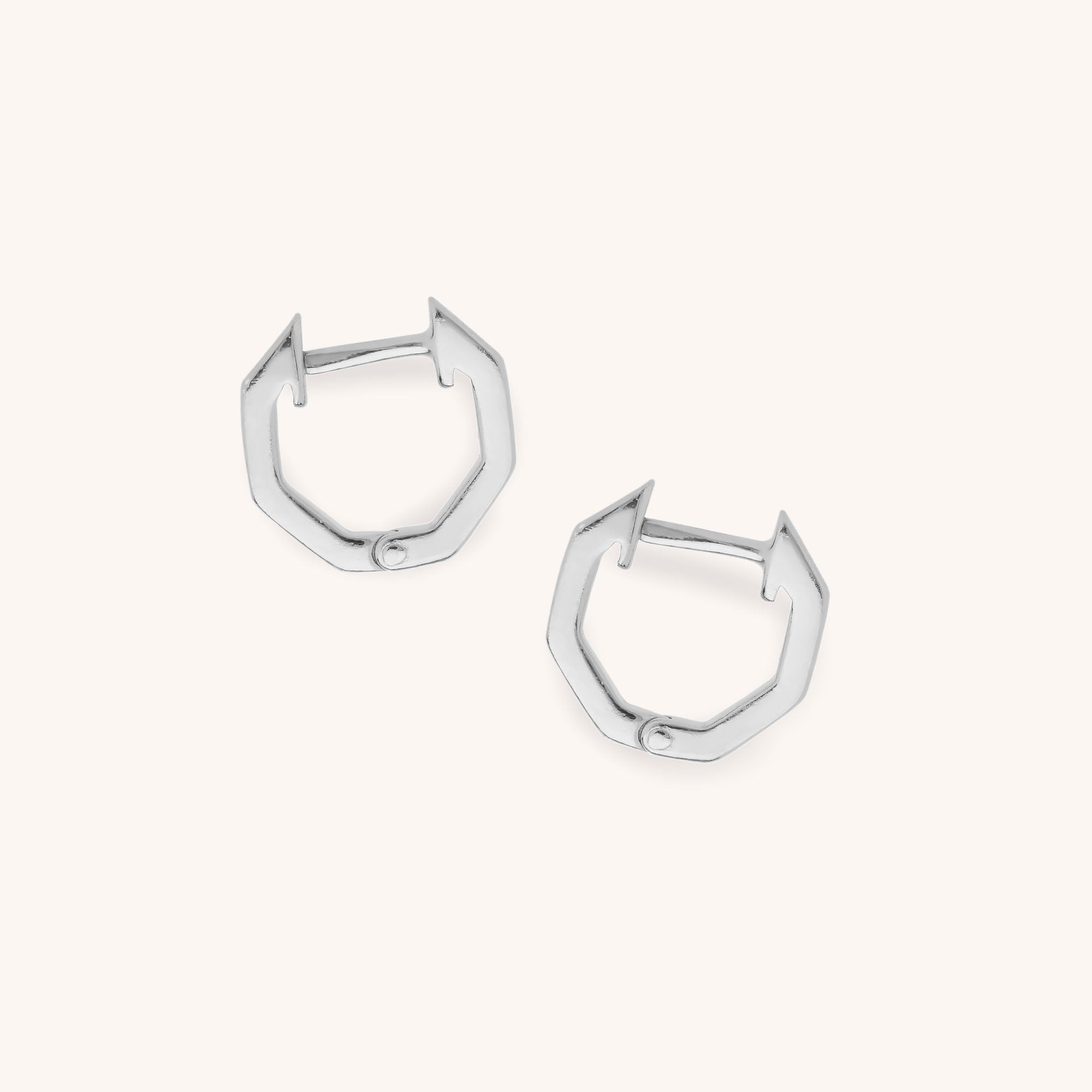 The Hex Huggie Earrings feature sterling silver hexagonal hoops with hinged clasps, highlighting geometric elegance against a light, neutral background.