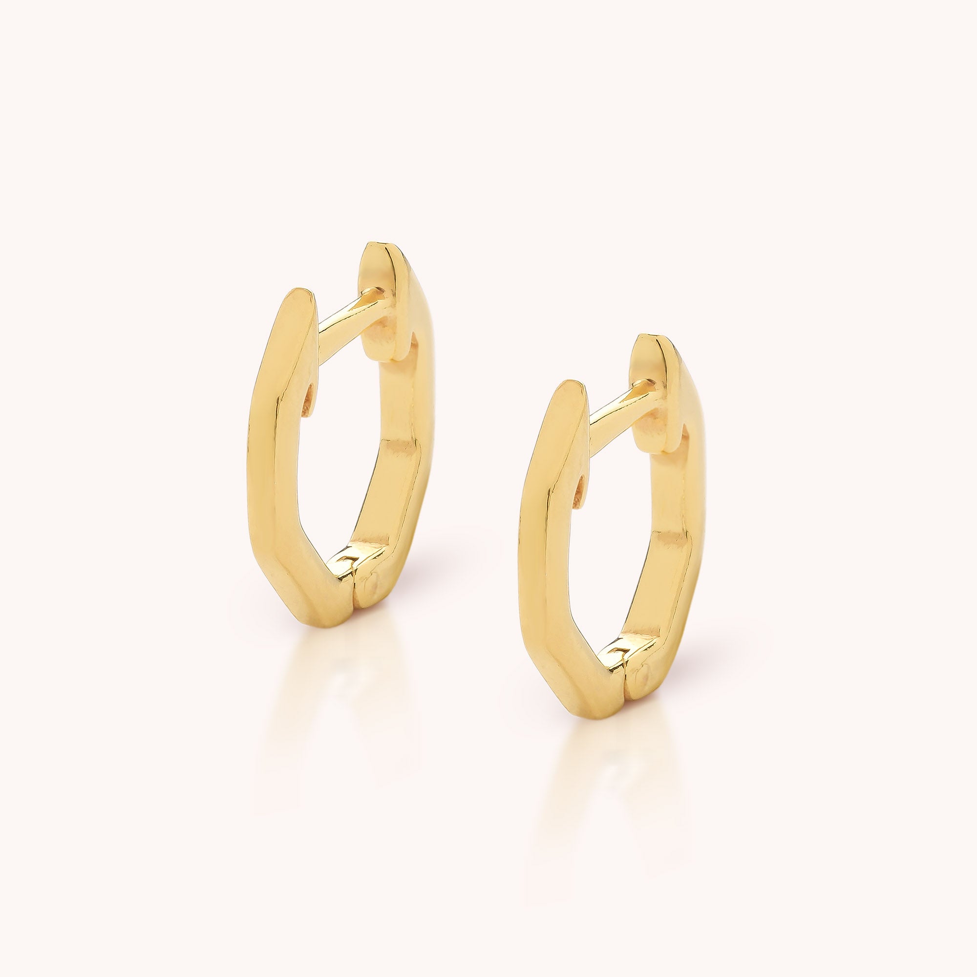 The Hex Huggie Earrings are small, hexagonal gold hoop earrings with a modern geometric design and a smooth, polished finish, shown on a plain light background.