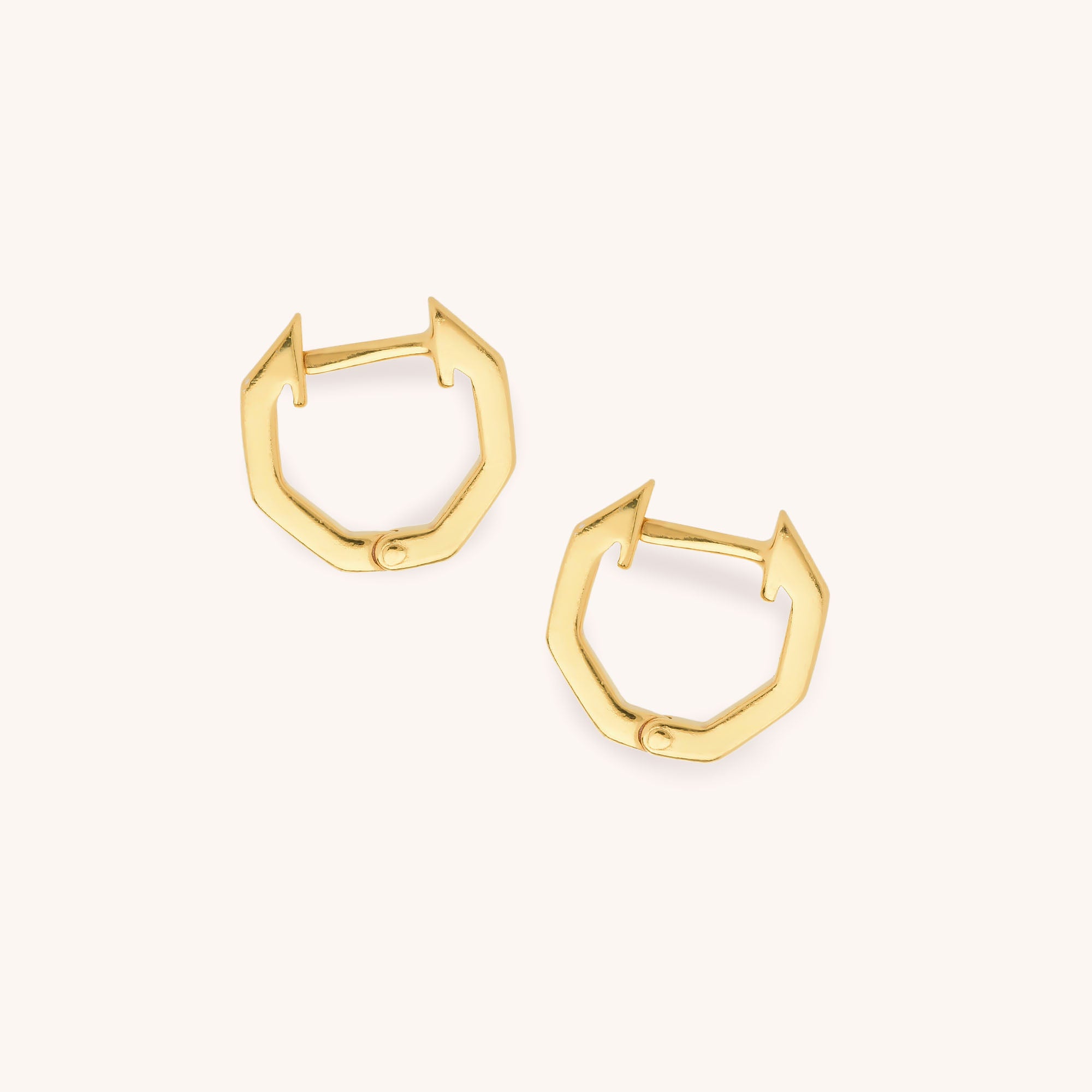 A pair of Hex Huggie Earrings in gold, featuring a hinged clasp and sleek geometric design, are displayed on a light beige background for an elegant look.