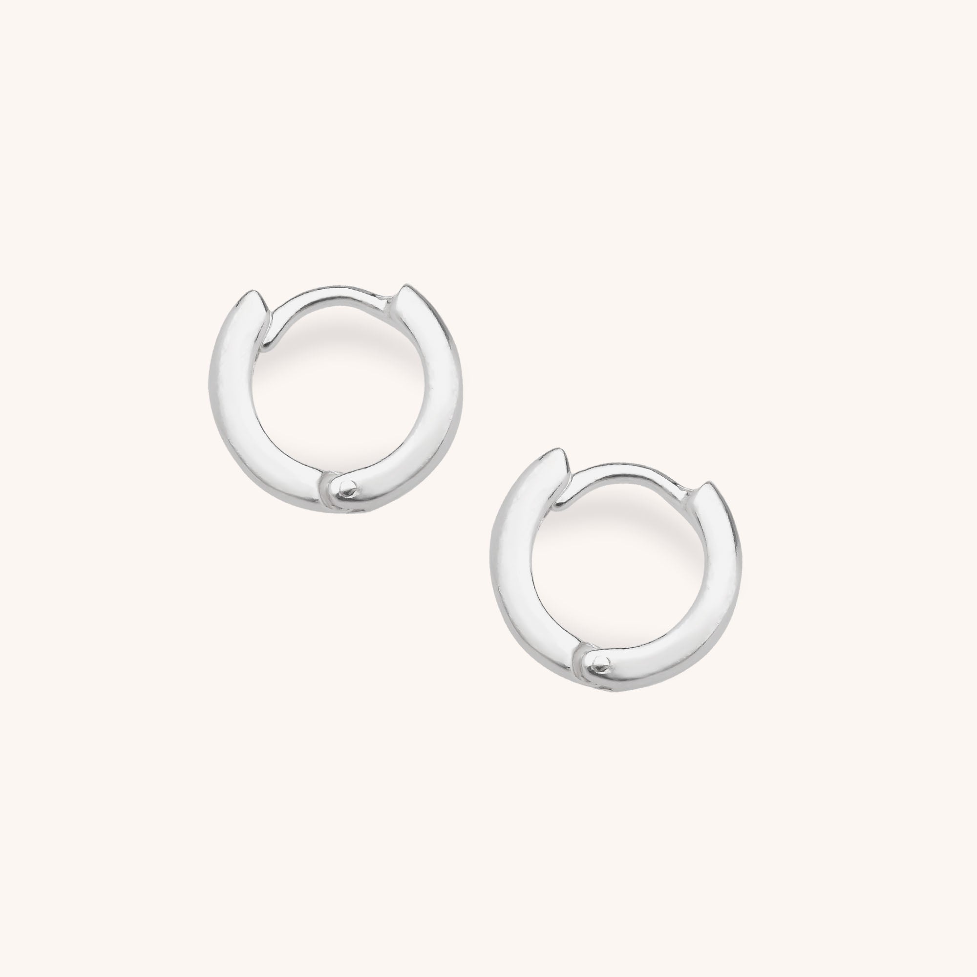 The Nell Huggie Earrings are small, sterling silver hoops with a smooth, shiny finish in a minimalist style, shown against a plain light background.