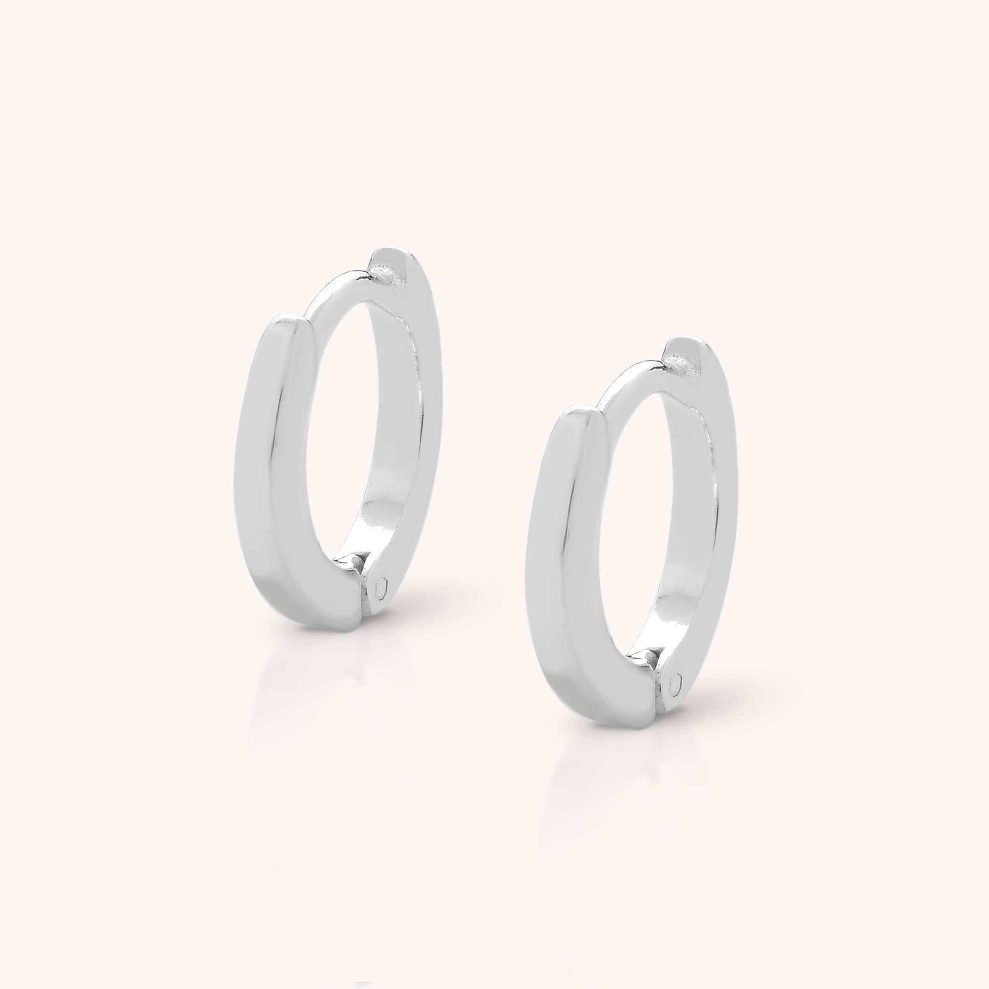 The Nell Huggie Earrings, crafted from polished sterling silver in a minimalist style, are displayed upright on a light, neutral background.