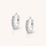 The Ava Huggie Earrings are small sterling silver hoops with clear cubic zirconia gemstones set along the front, shown on a plain light background.