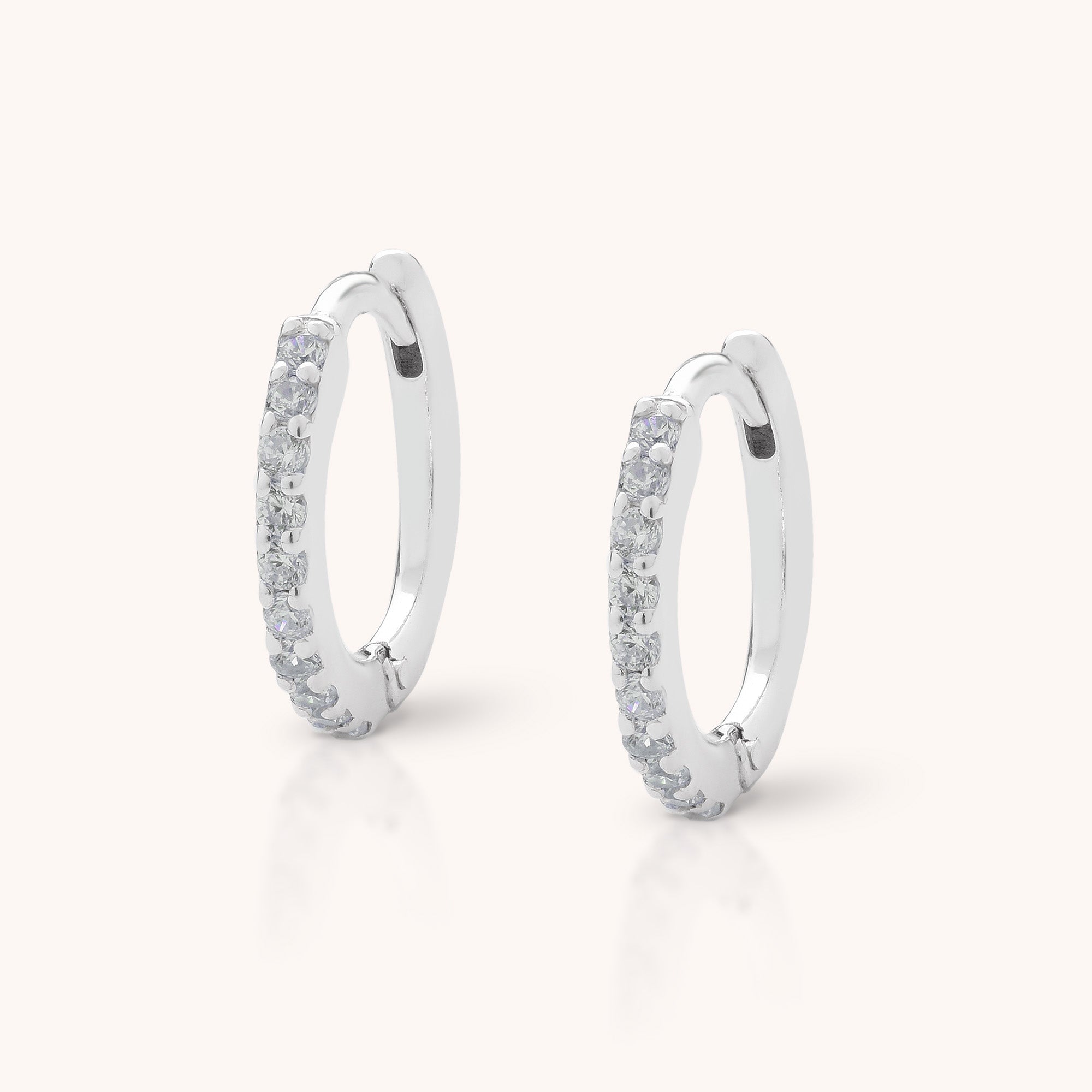 The Ava Huggie Earrings are small sterling silver hoops, each featuring a row of sparkling cubic zirconia on the front, shown against a plain light background.