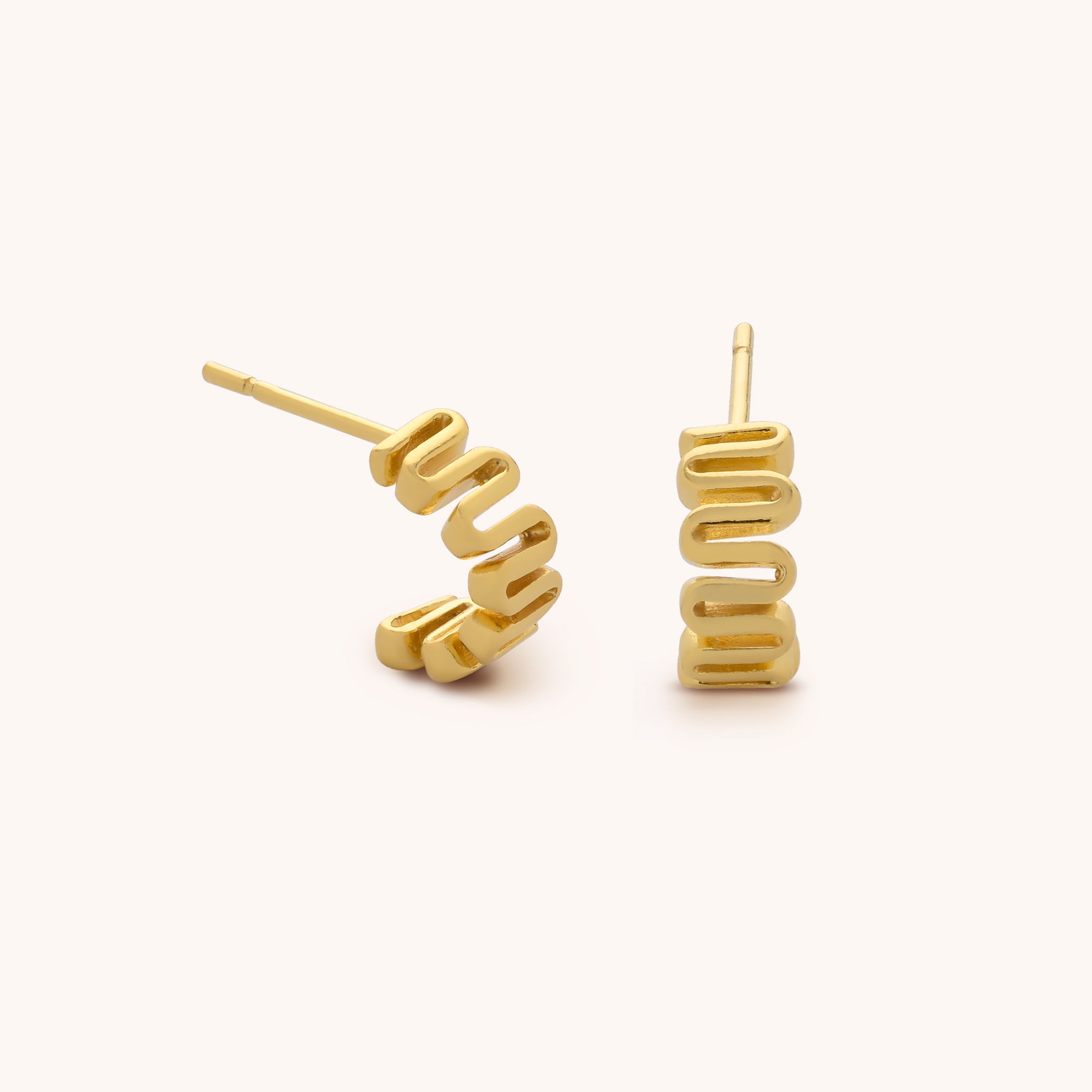 The Wiggle Hoop Earrings are 18ct gold plated with a wavy zigzag design. One stands upright and the other lies on its side, showcasing their unique shape and shiny finish against a plain background.
