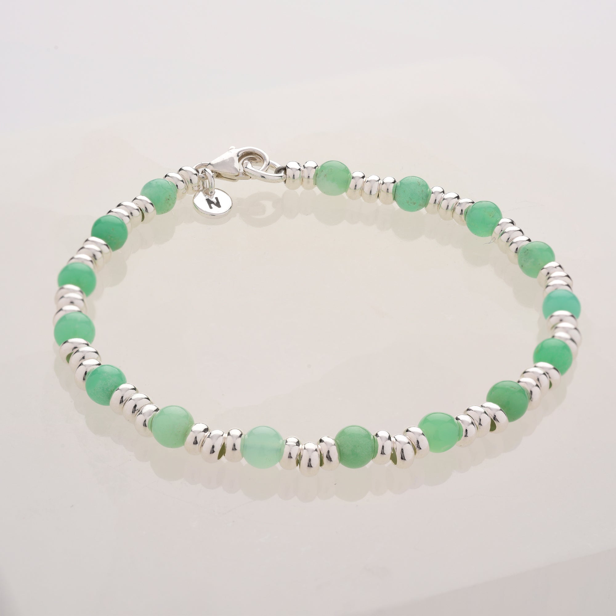 The Gem Bracelet May Birthstone features alternating small silver beads and light green Chrysoprase rounds, finished with a silver lobster clasp and a round charm—an ideal accessory for those born in May.