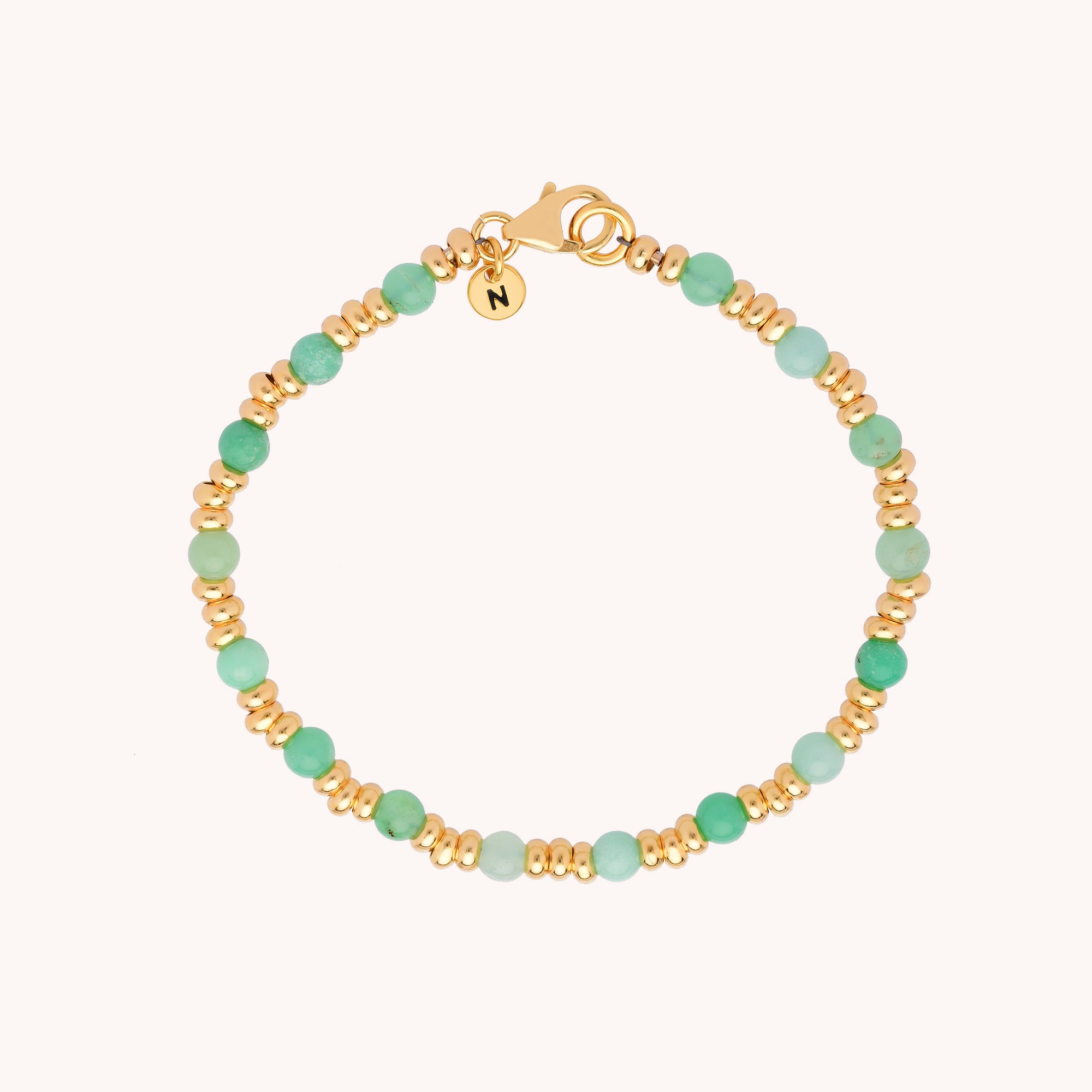 The Gem Bracelet May Birthstone features alternating gold and Chrysoprase green beads, a small gold charm engraved with N near the clasp, and is beautifully displayed on a light background.