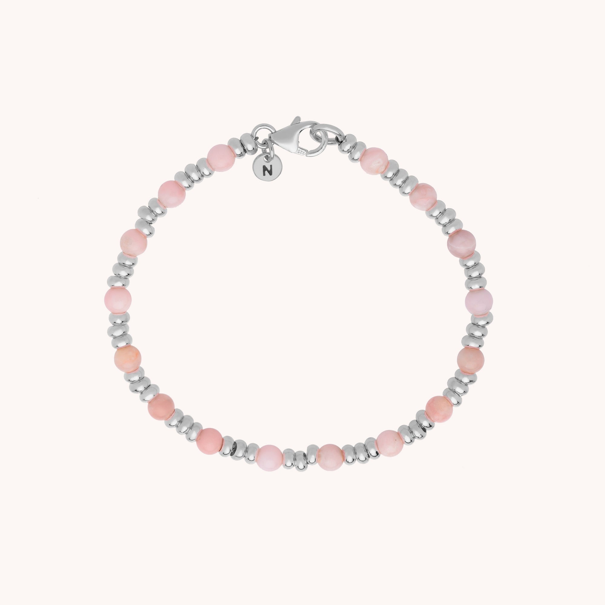 The Gem Bracelet October Birthstone features alternating Pink Opal beads for emotional healing, eco-silver spacers, a silver clasp, and a round charm engraved with “N.”.