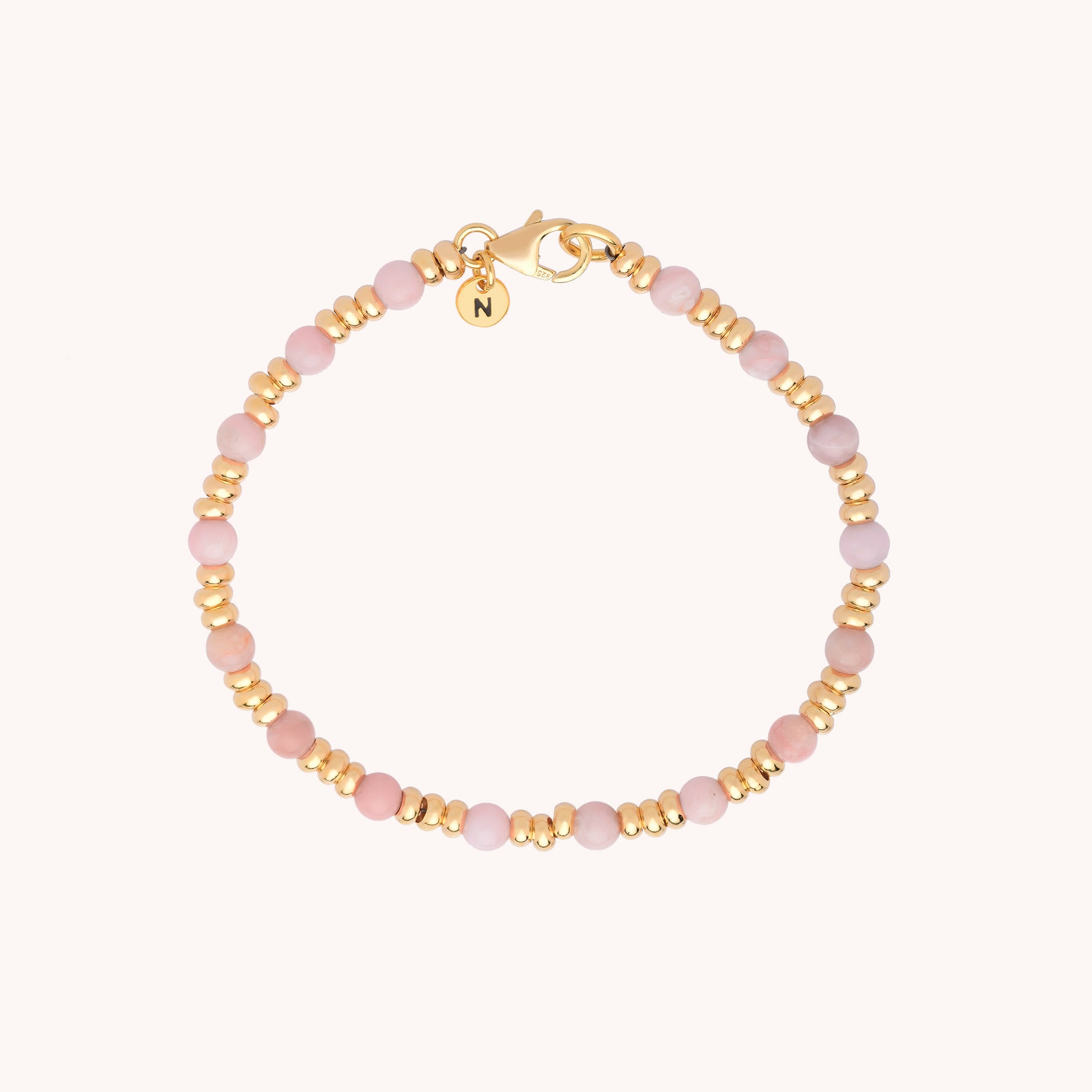 The Gem Birthstone Bracelet features alternating small pink natural gemstone and gold beads, a gold clasp, and a round gold charm engraved with the letter N—ideal for those who love birthstone jewelry with a personal touch.