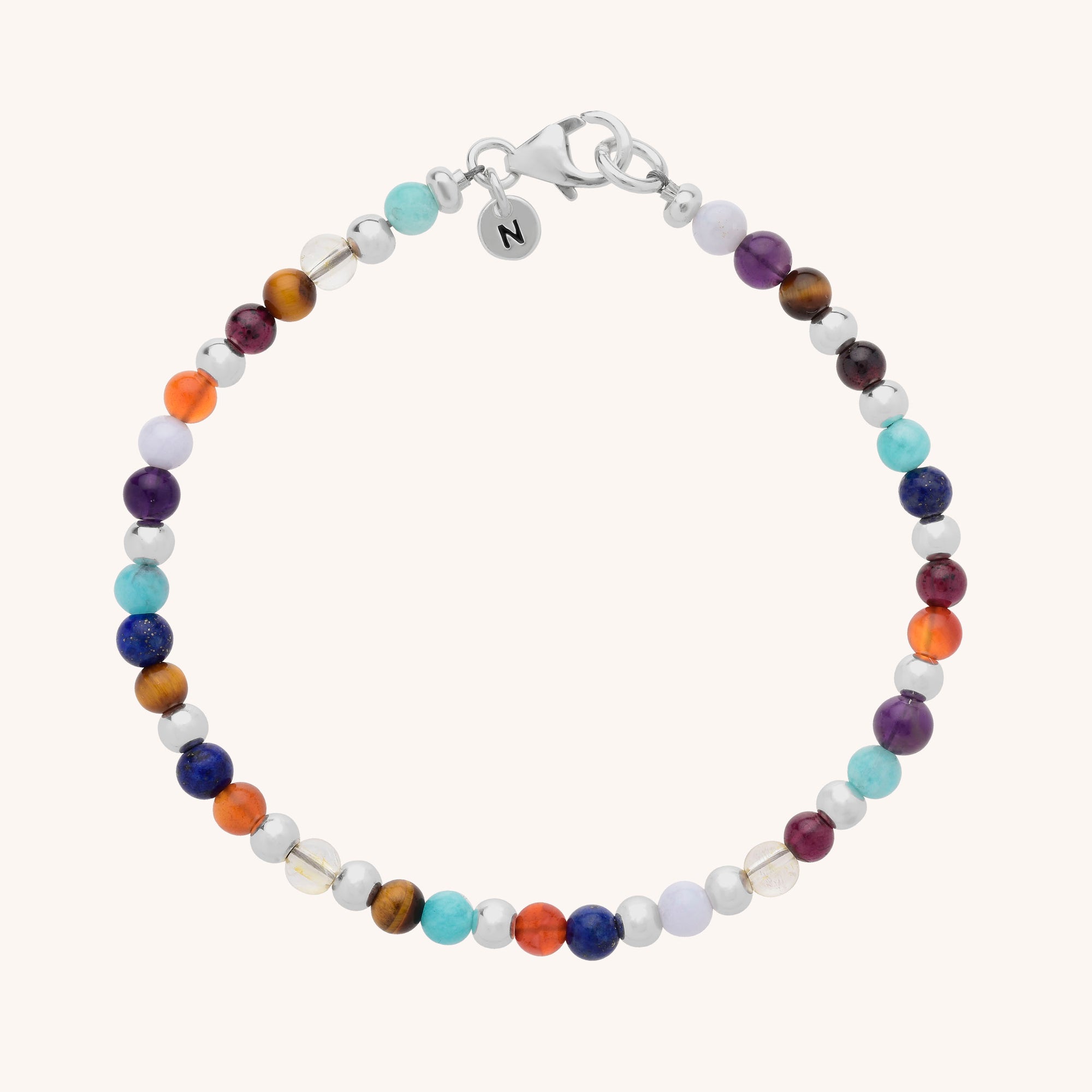 The Multi Gemstone Bracelet showcases blue, red, orange, purple, and brown round semi-precious beads with small silver accents and a silver clasp featuring an engraved N charm.
