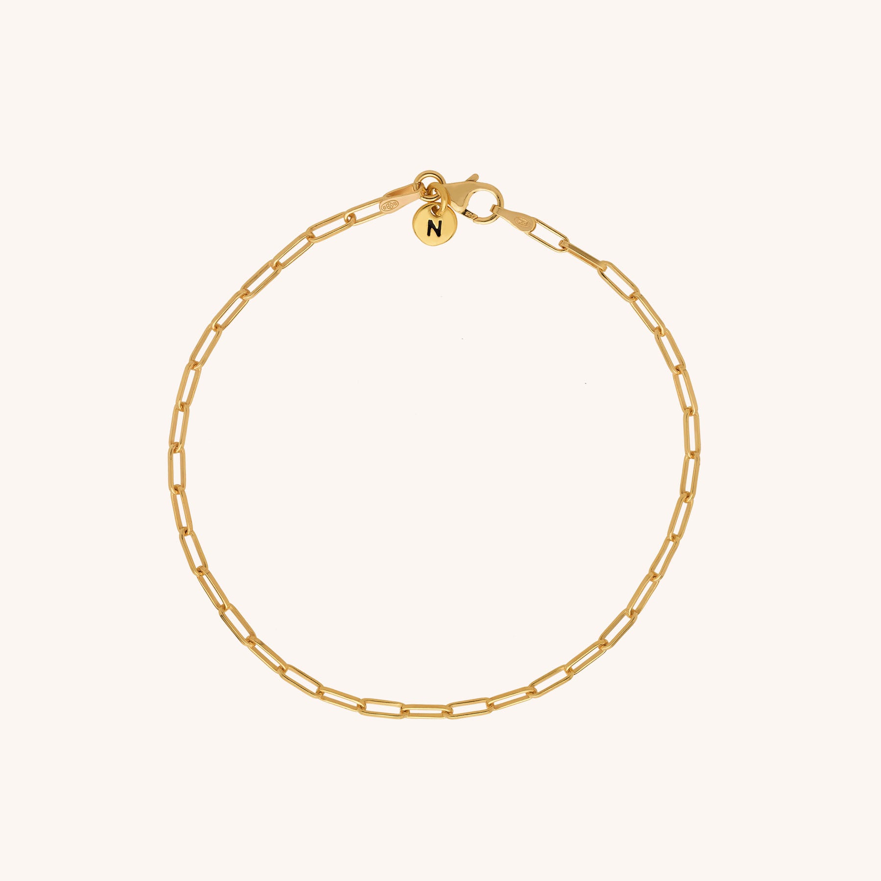 The Baby Paperclip Bracelet is a delicate gold chain with elongated links and a small round N charm near the clasp, displayed on a simple light background.