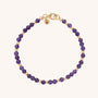 The Jewel Bead Birthstone Bracelet - February features alternating amethyst and gold beads, finished with a gold lobster clasp and a round gold tag engraved with the letter N.