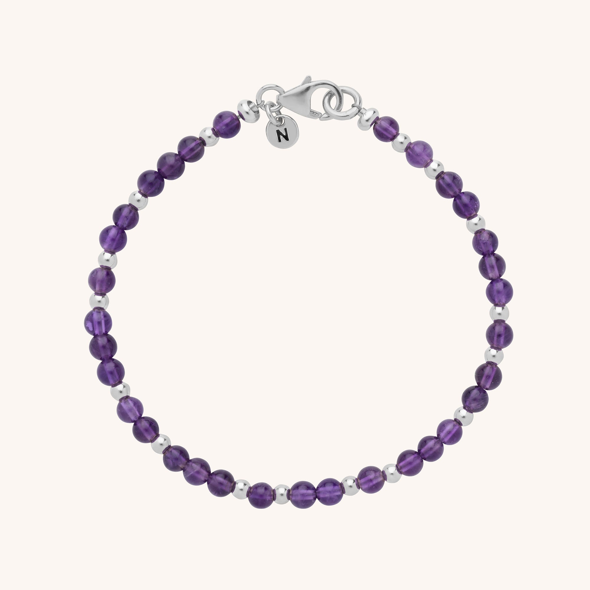 The Jewel Bead Birthstone Bracelet features alternating purple and silver beads, a silver lobster clasp, and a round charm with the letter N—an ideal handmade gift for jewellery lovers.