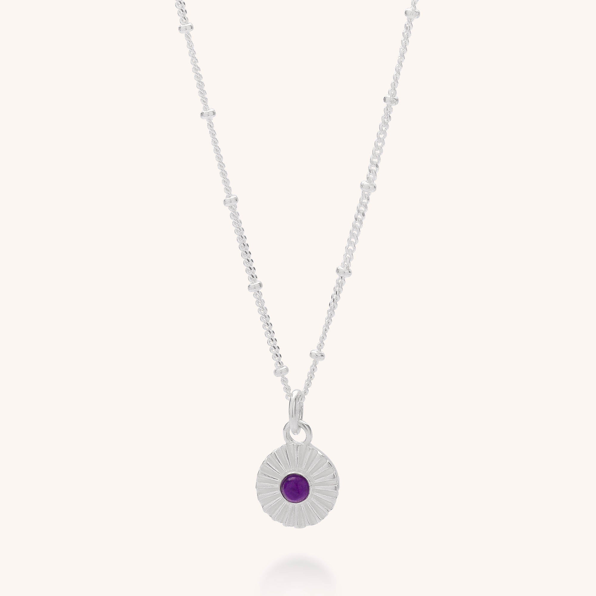 The Radiance Birthstone Necklace - February is a sterling silver necklace with a delicate beaded chain and a round sunburst pendant featuring a central Amethyst for emotional balance.