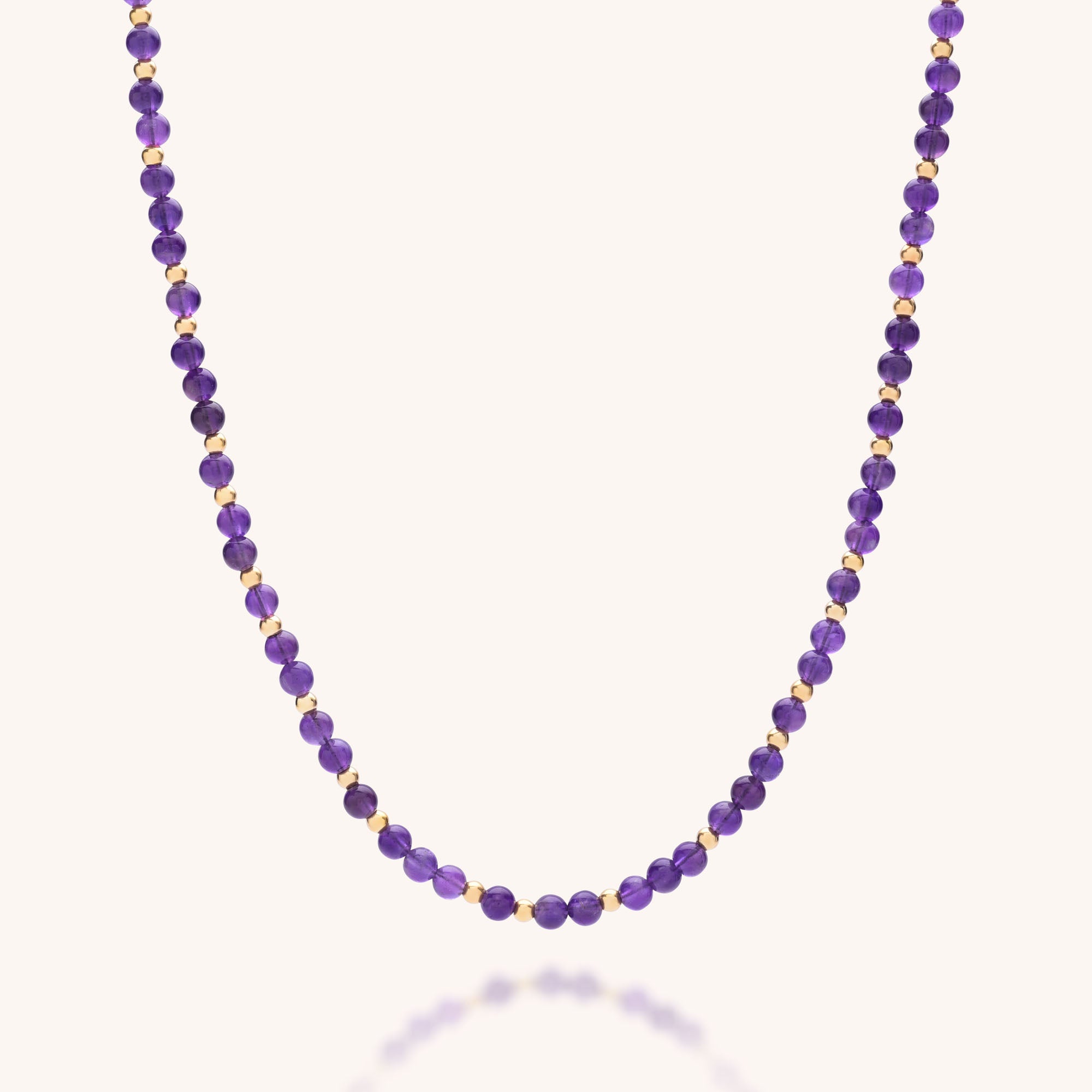 The Jewel Bead Birthstone Necklace - February features small, round Amethyst beads and gold accents on a sterling silver strand, creating a simple and elegant piece.