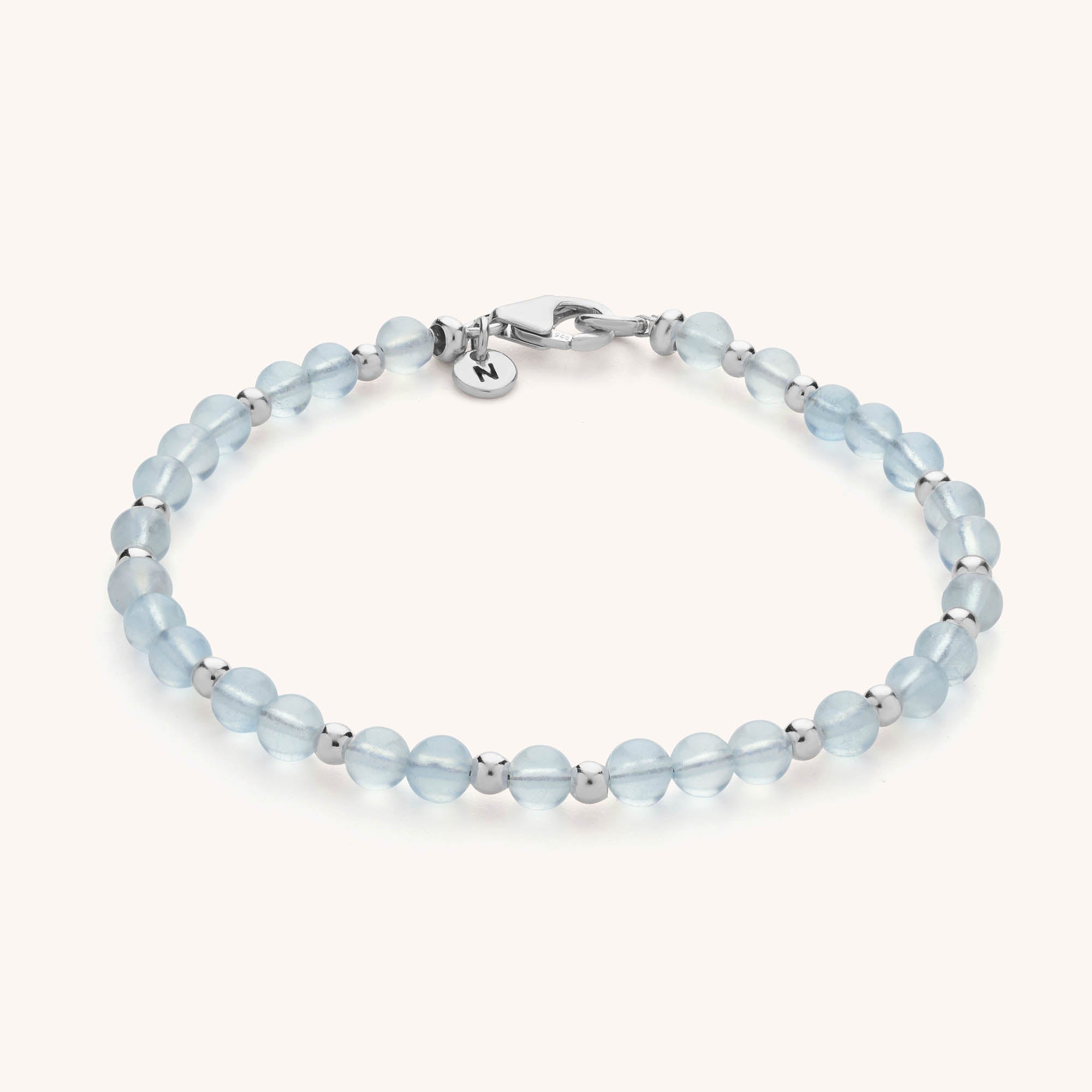 The Jewel Bead Birthstone Bracelet - March features light blue translucent aquamarine gemstones, eco-friendly sterling silver spacer beads, a silver lobster clasp, and a round charm, beautifully arranged on a light background.