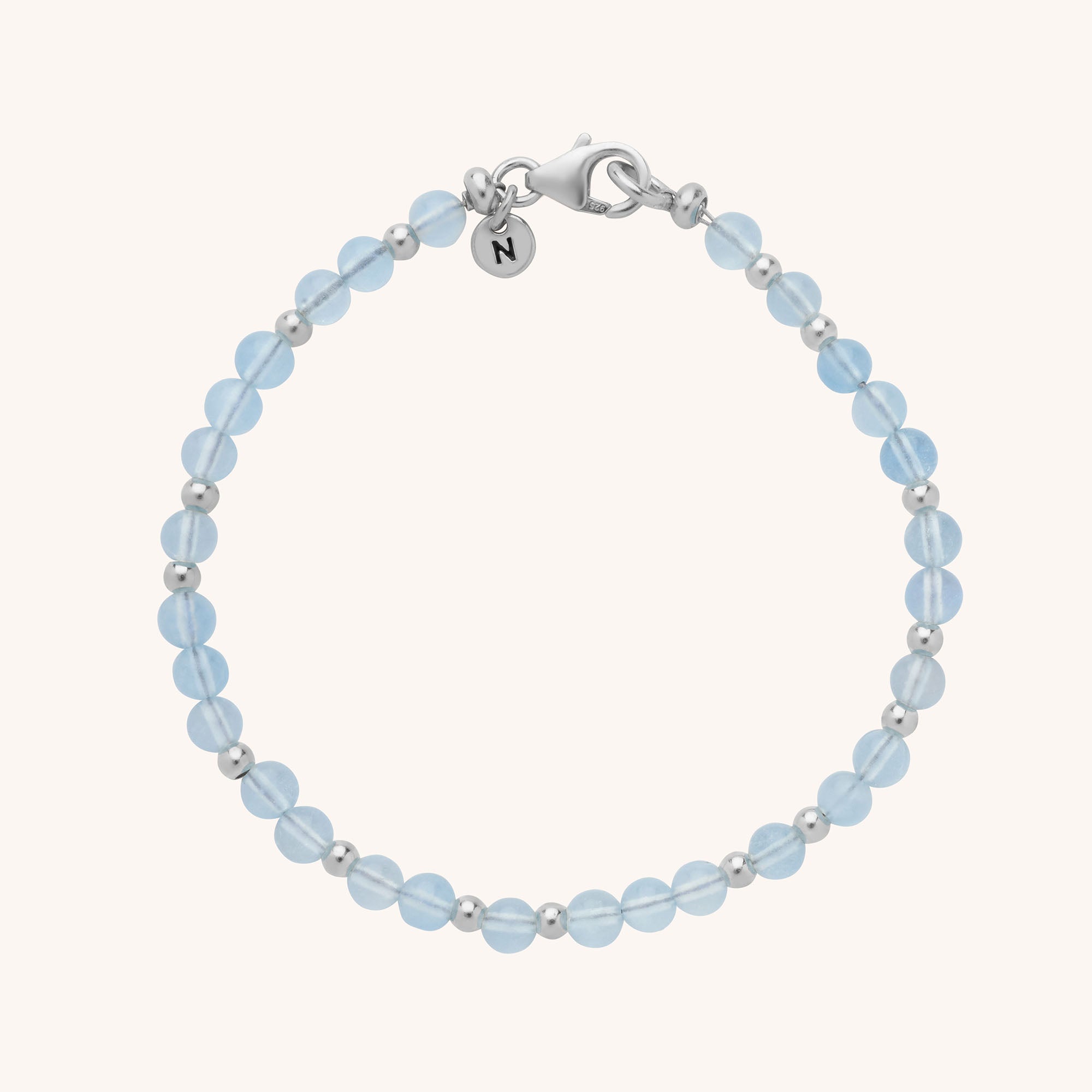 The Jewel Bead Birthstone Bracelet - March features alternating round aquamarine gemstones and eco-friendly sterling silver beads, finished with a silver lobster clasp and a small round charm engraved with the letter N.