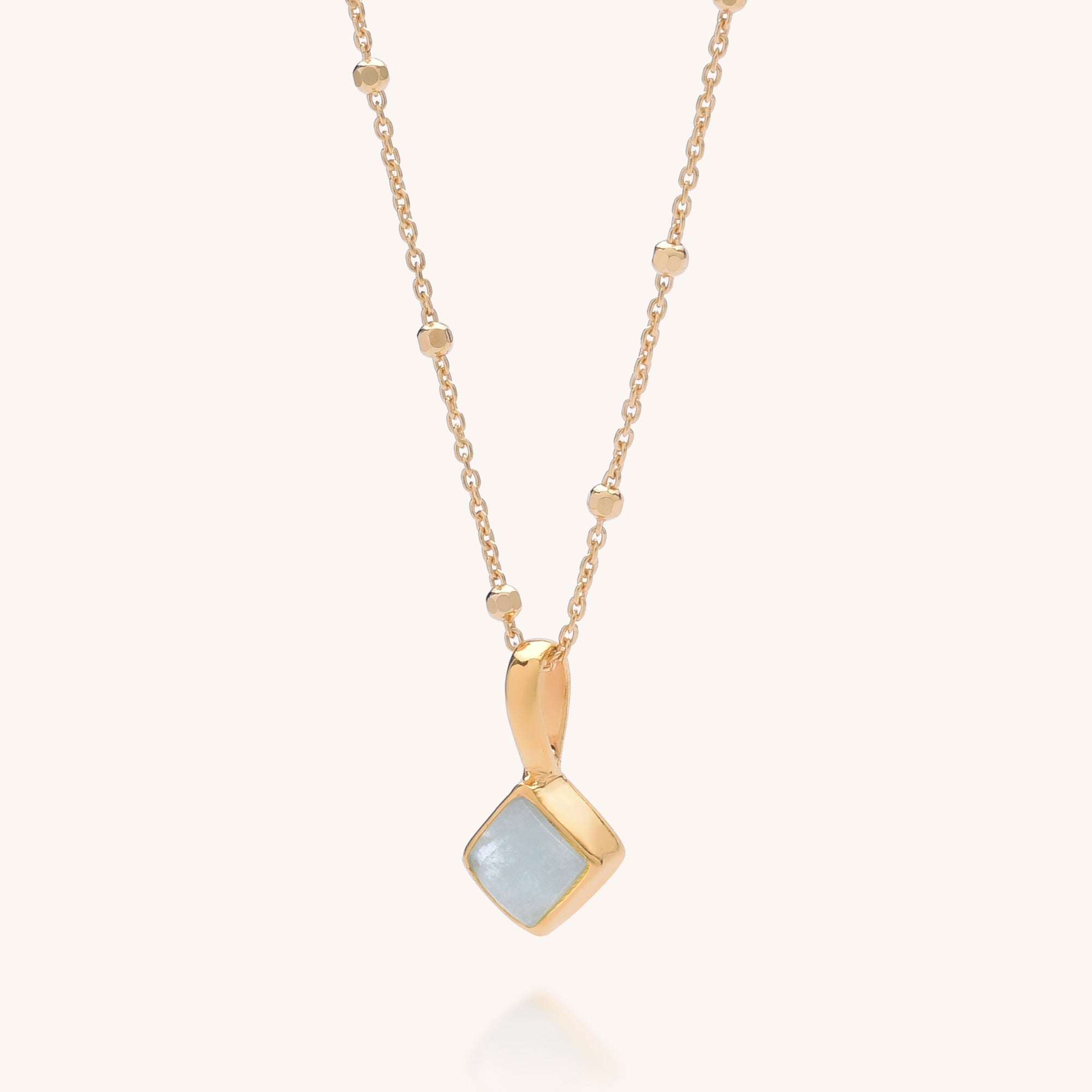 The Diamond Birthstone Necklace March features a gold chain with small beads and a square Aquamarine pendant, the March birthstone, set in gold and displayed against a plain light background.