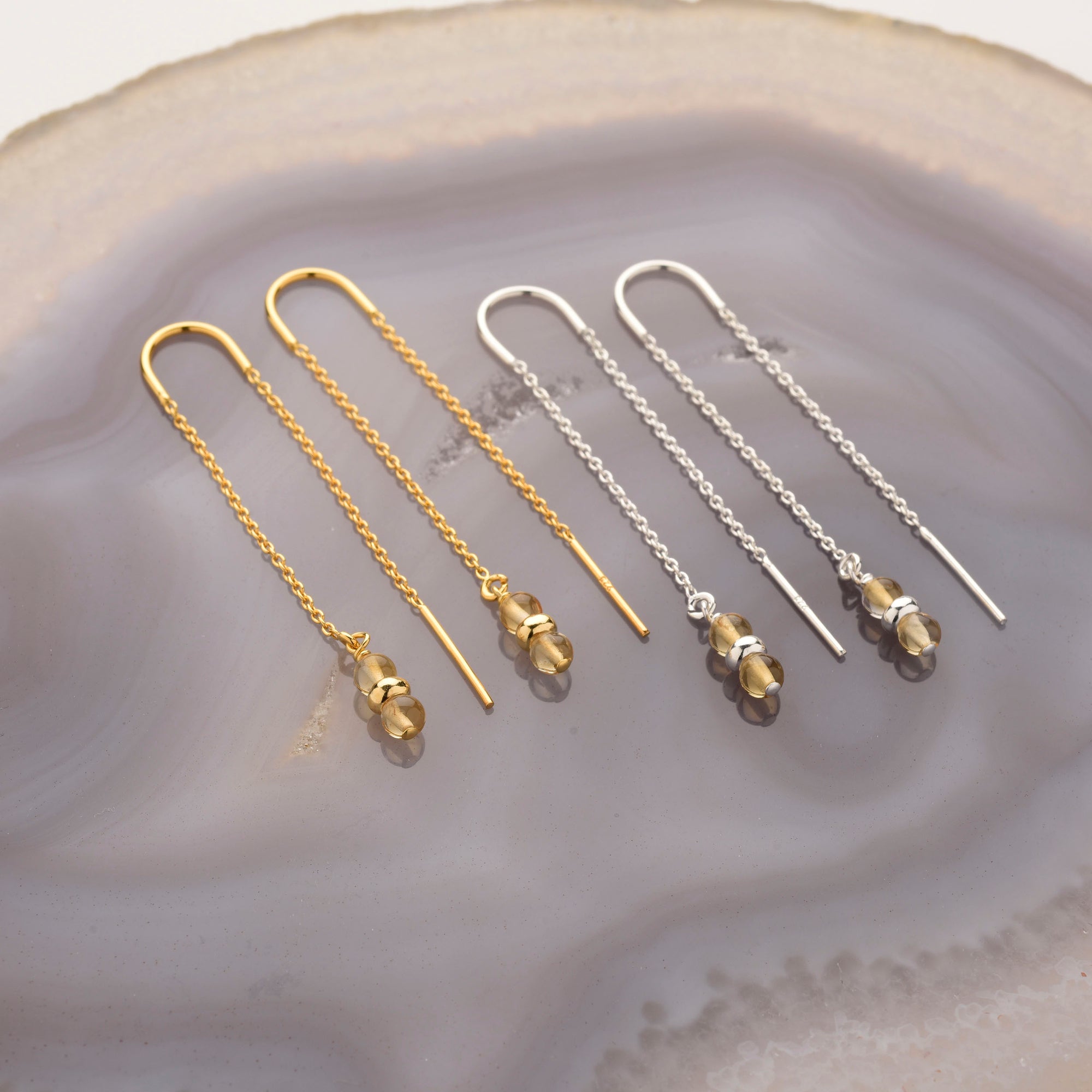 Two pairs of Fall Earrings Birthstone November—one gold, one silver—with thin chains and Citrine gemstone beads, displayed on a smooth agate-like surface; perfect birthstone jewelry for November.