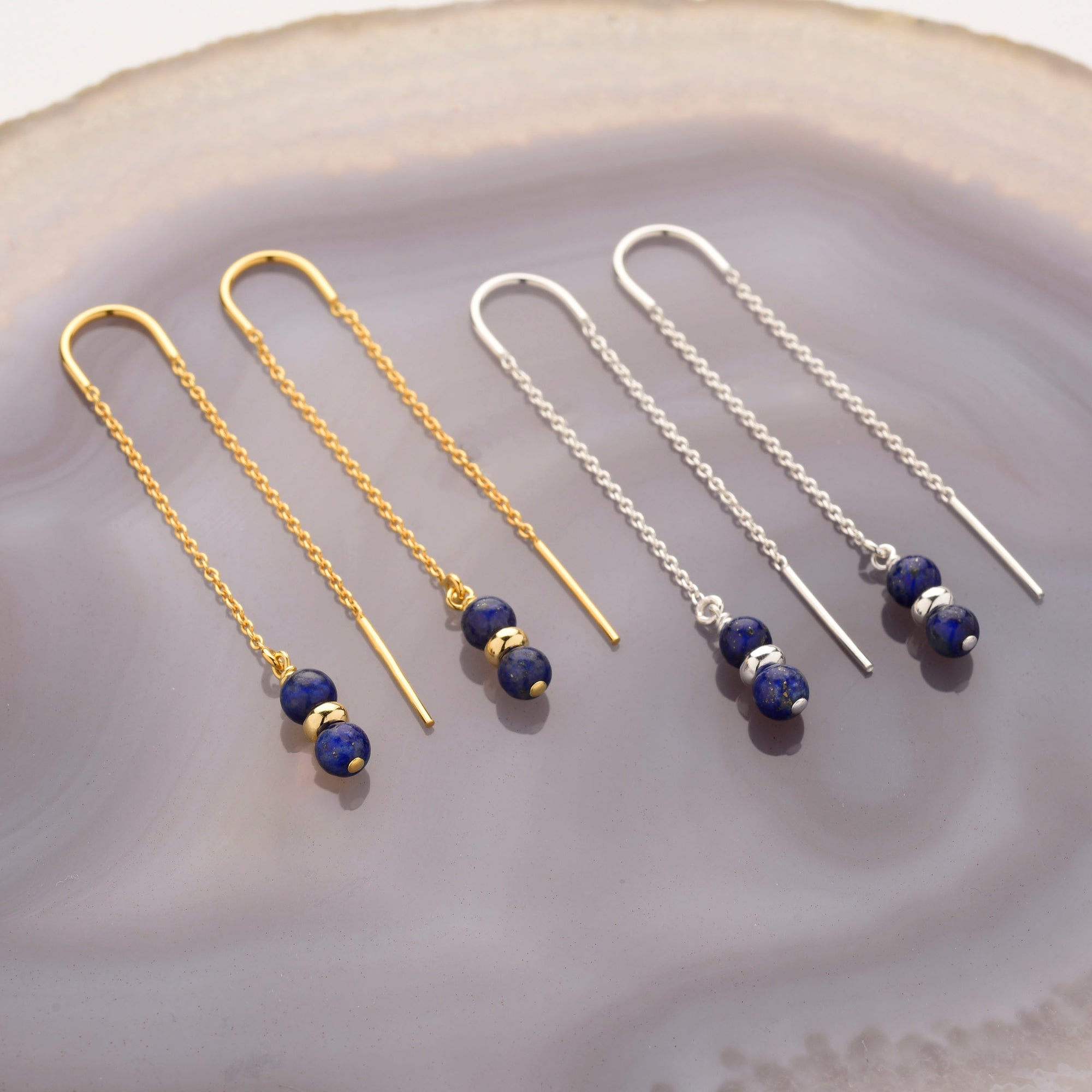 The Fall Earrings Birthstone September feature gold and silver threaders with denim blue beads, side by side on a polished gray agate slab. Each earring has two lapis lazuli-like beads separated by a metallic accent.