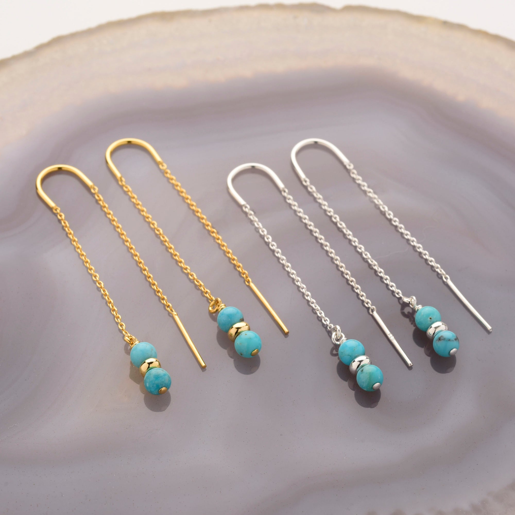 Two pairs of Fall Earrings Birthstone December are displayed on a polished stone surface—one gold pair with turquoise and gold beads, and another sterling silver pair with turquoise and silver beads.