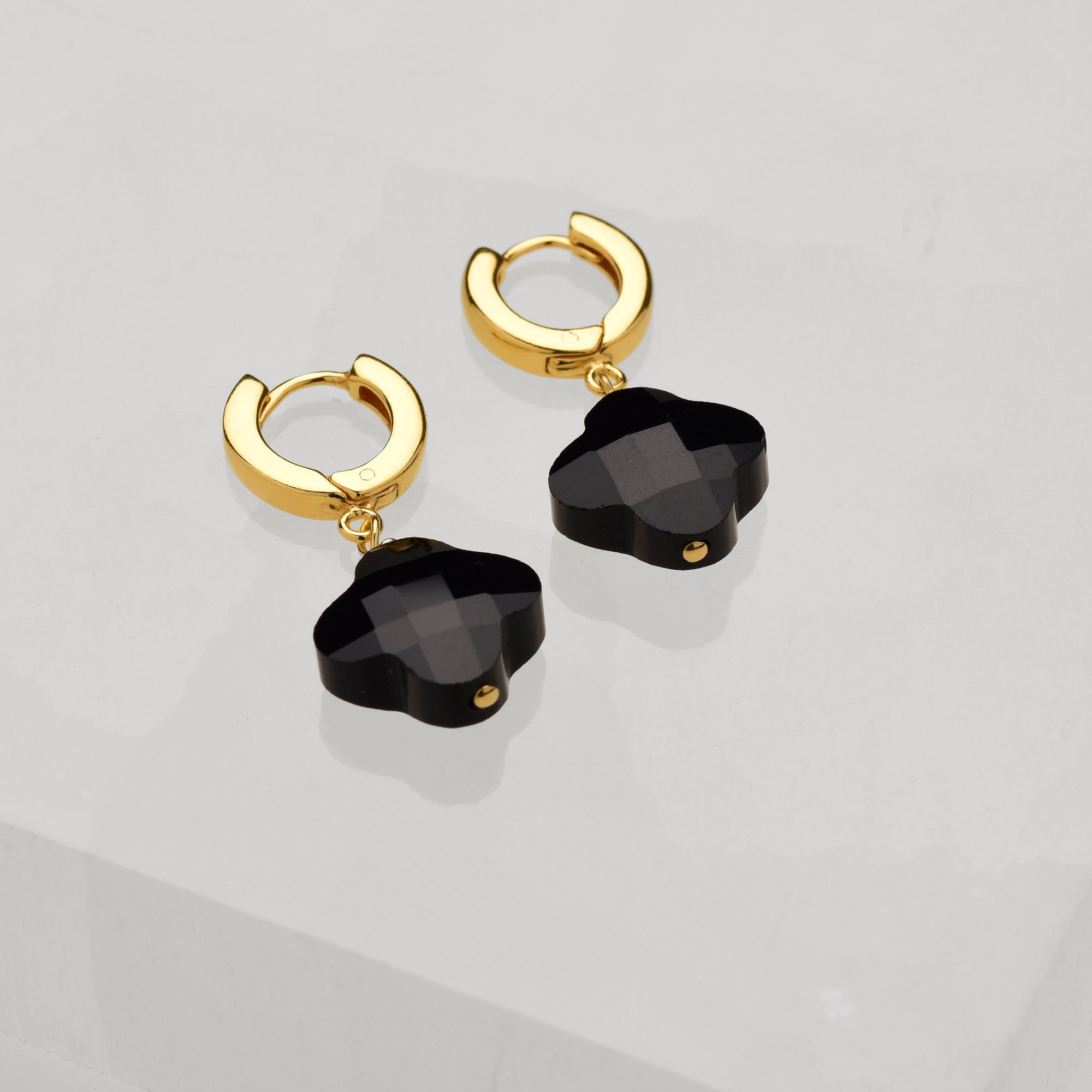 A pair of Clover Gem Hoop Earrings in gold with faceted black gemstone pendants, shown on a glossy light gray surface.
