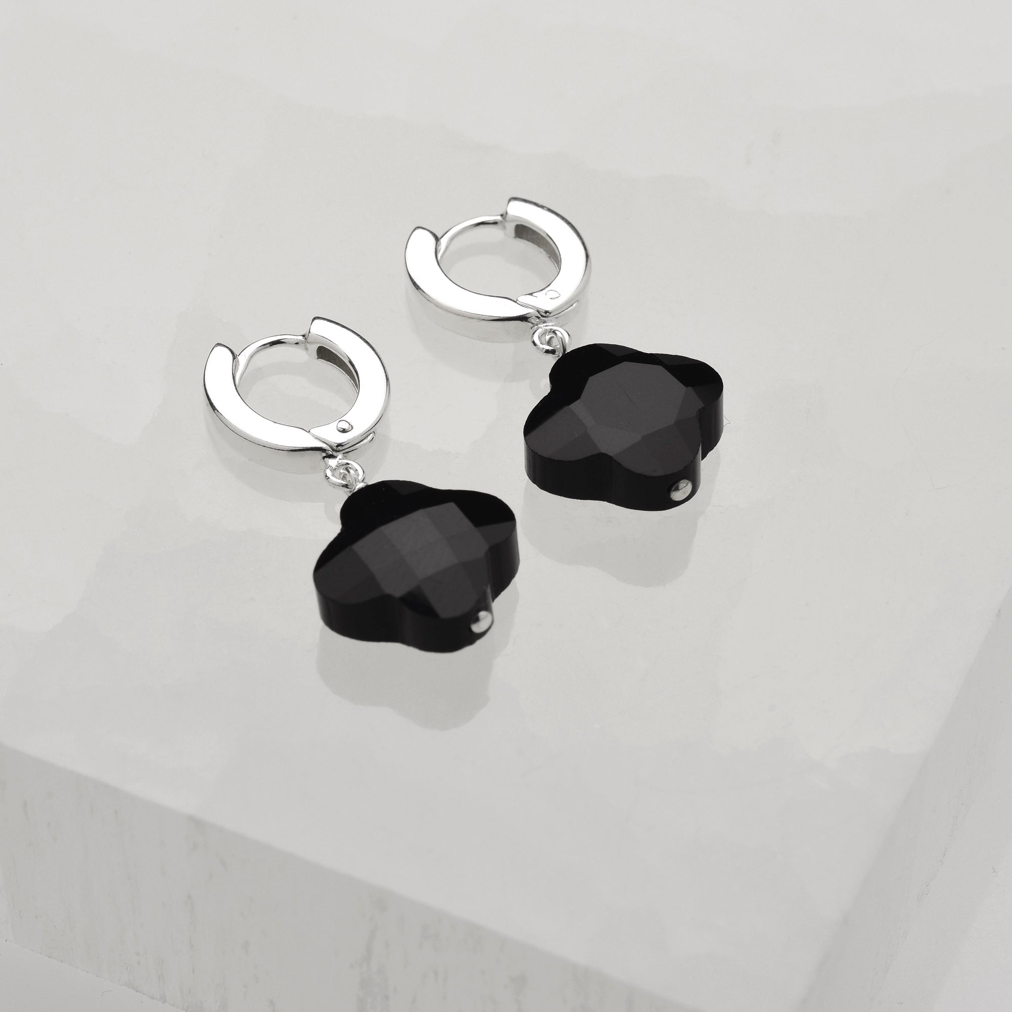 Clover Gem Hoop Earrings—sterling silver hoops with dangling black clover-shaped charms, shown on a white textured surface.