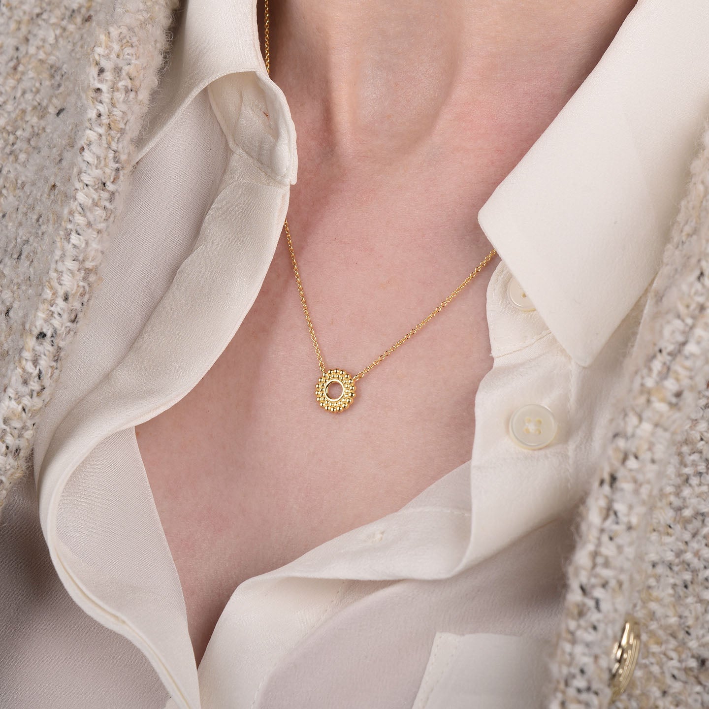 A woman in a cream blouse and beige jacket wears the Beaded Halo Necklace, an 18ct gold plated piece featuring a delicate circular pendant with small gemstones.