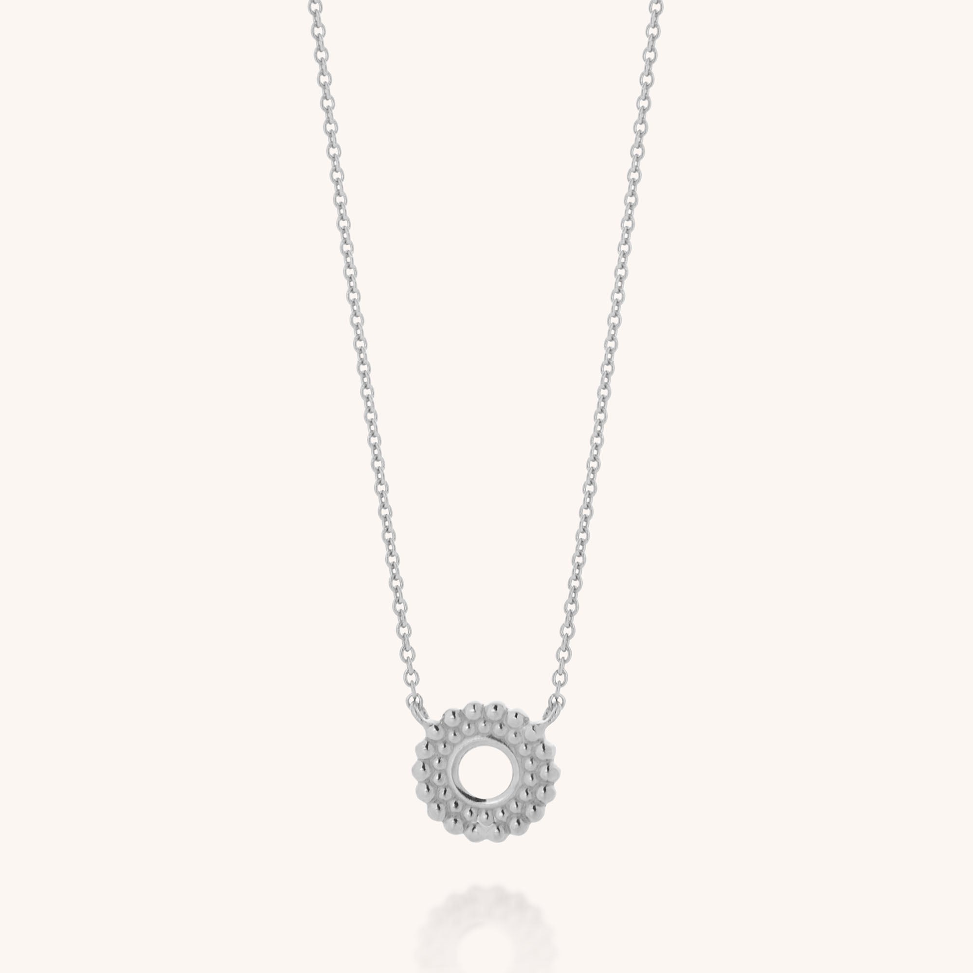 The Beaded Halo Necklace features a sterling silver, textured circular pendant on a fine chain, displayed against a plain light background.