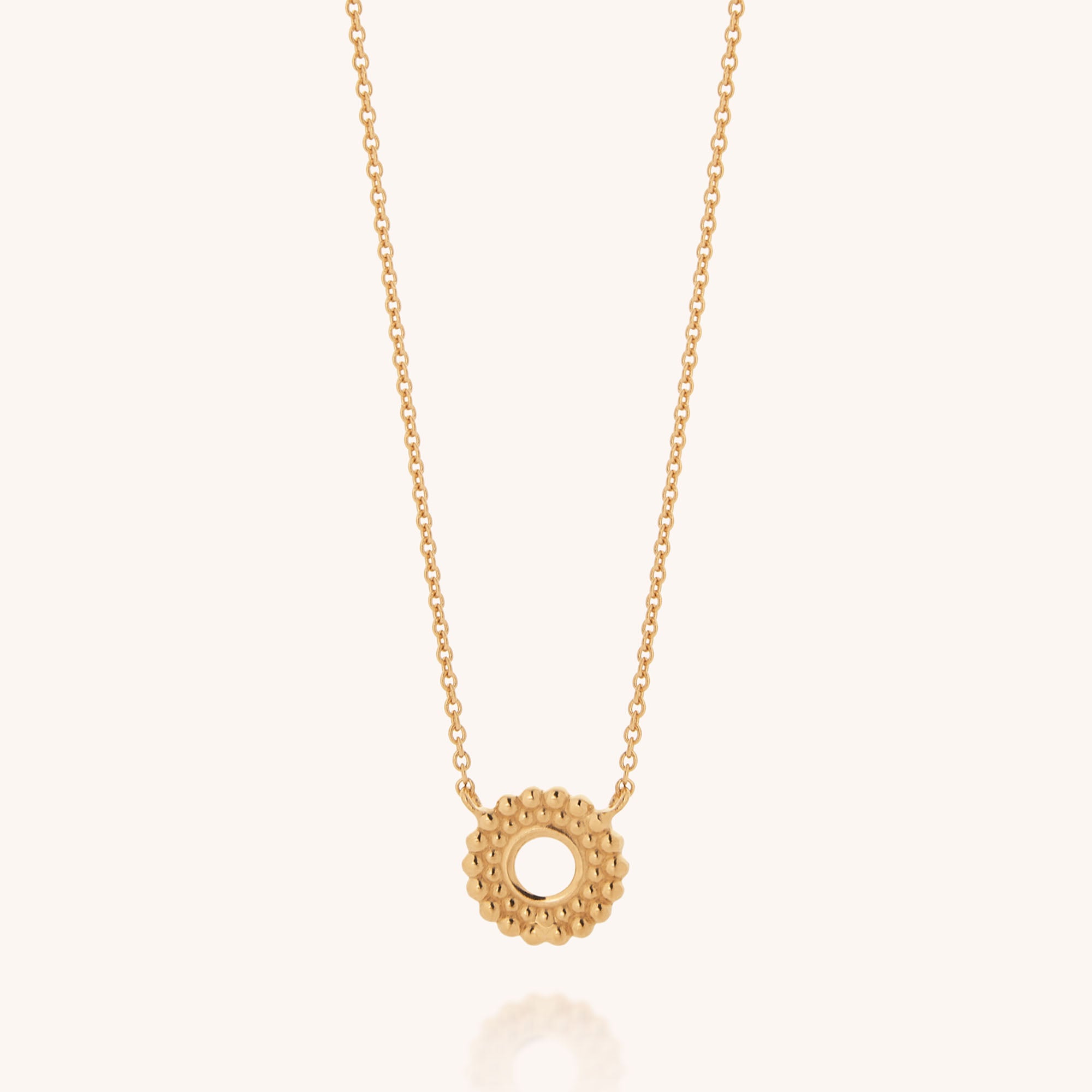 The Beaded Halo Necklace showcases a textured, circular pendant with a hollow center on an 18ct gold plated chain, presented against a plain light background.